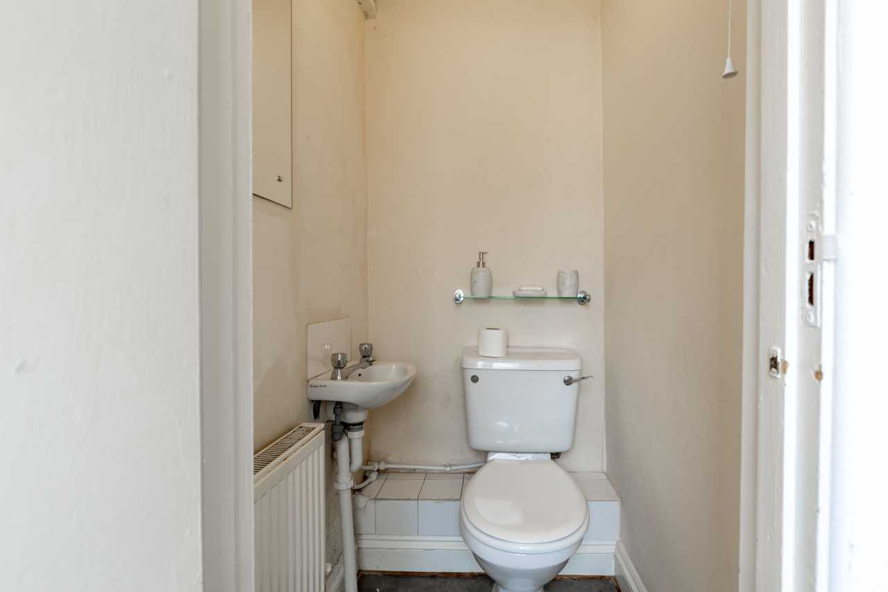Small bathroom with a toilet, pedestal sink, radiator and wall-mounted shelf.
