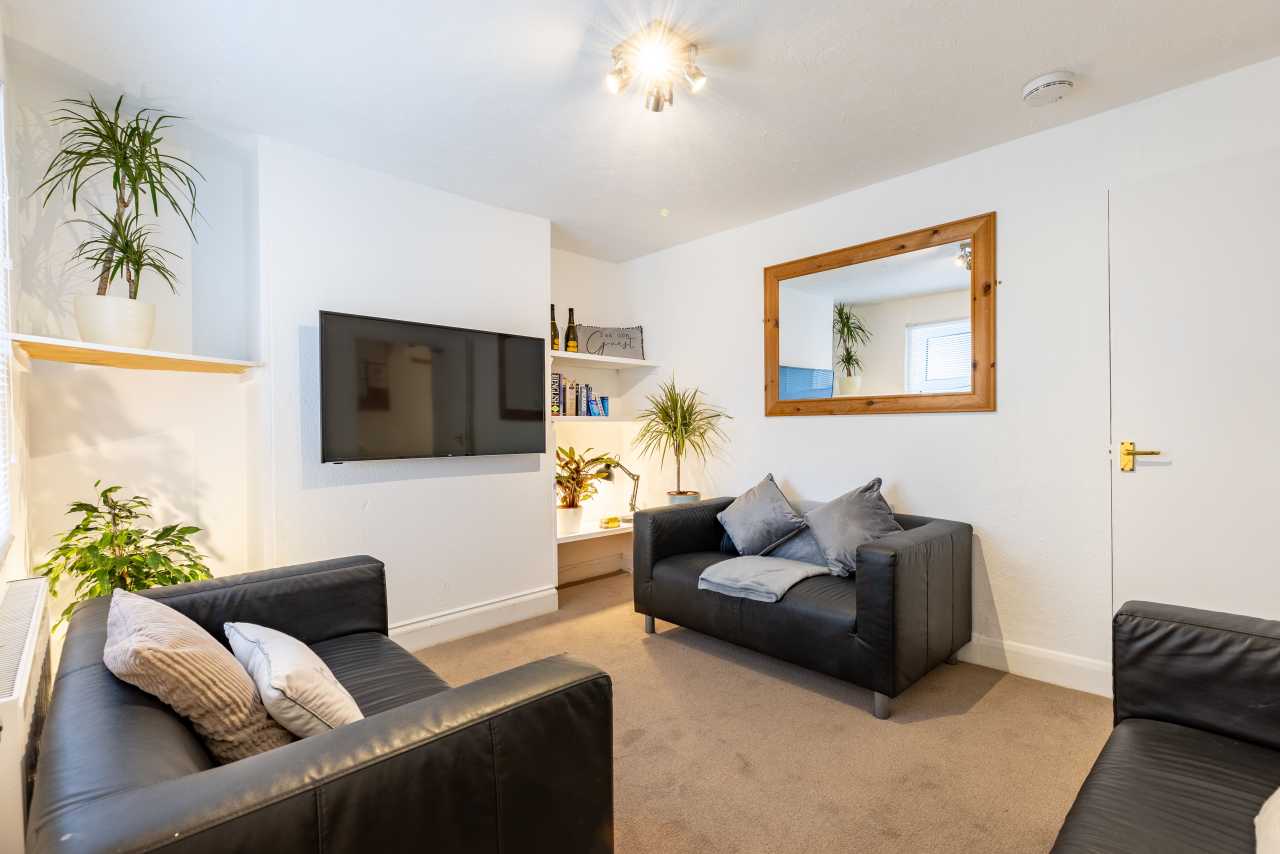 A furnished communal lounge with black sofas, a wall-mounted television, plants, shelving and a large wall mirror.