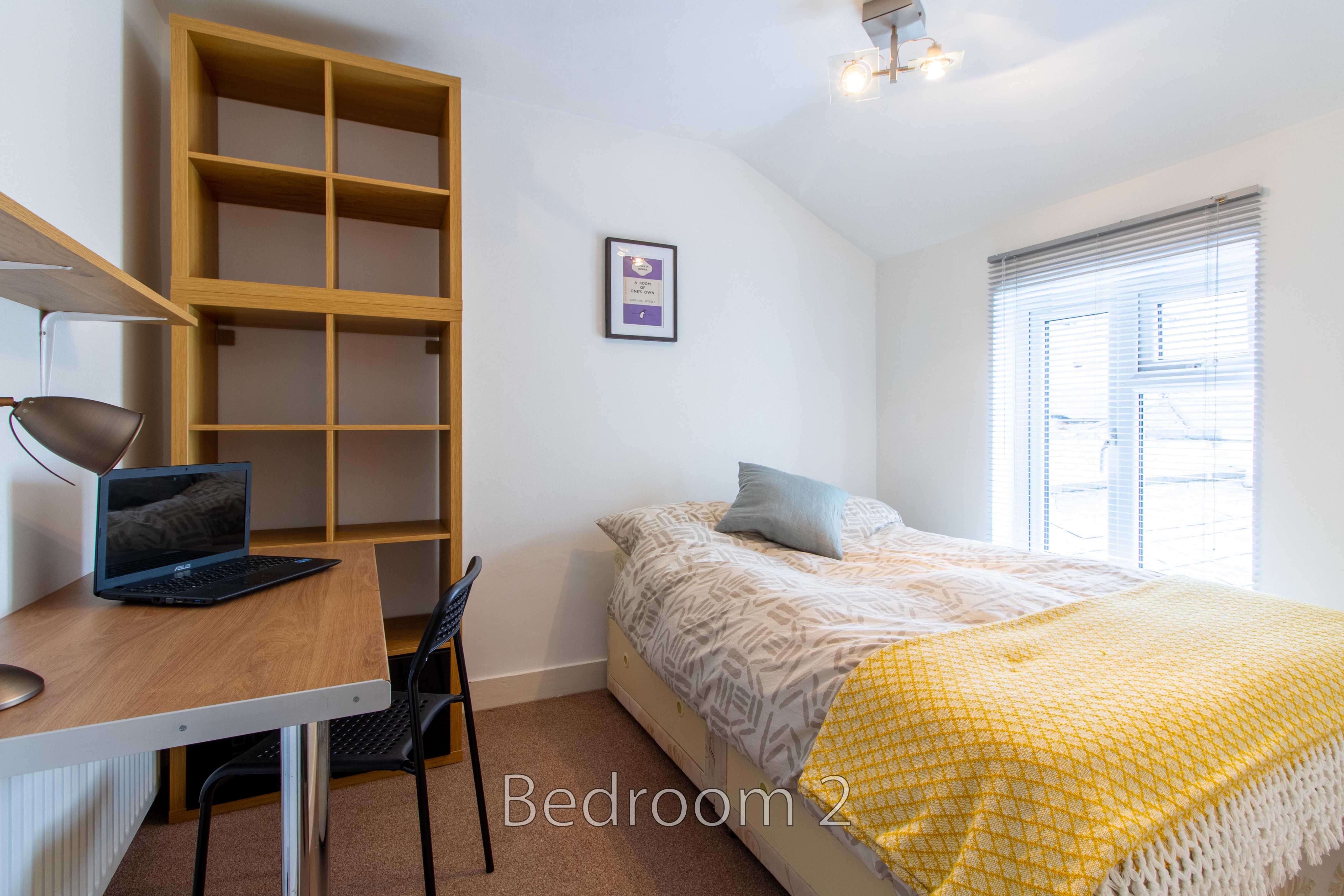 Bedroom with a bed, desk and chair, shelving, window blinds and a ceiling light.