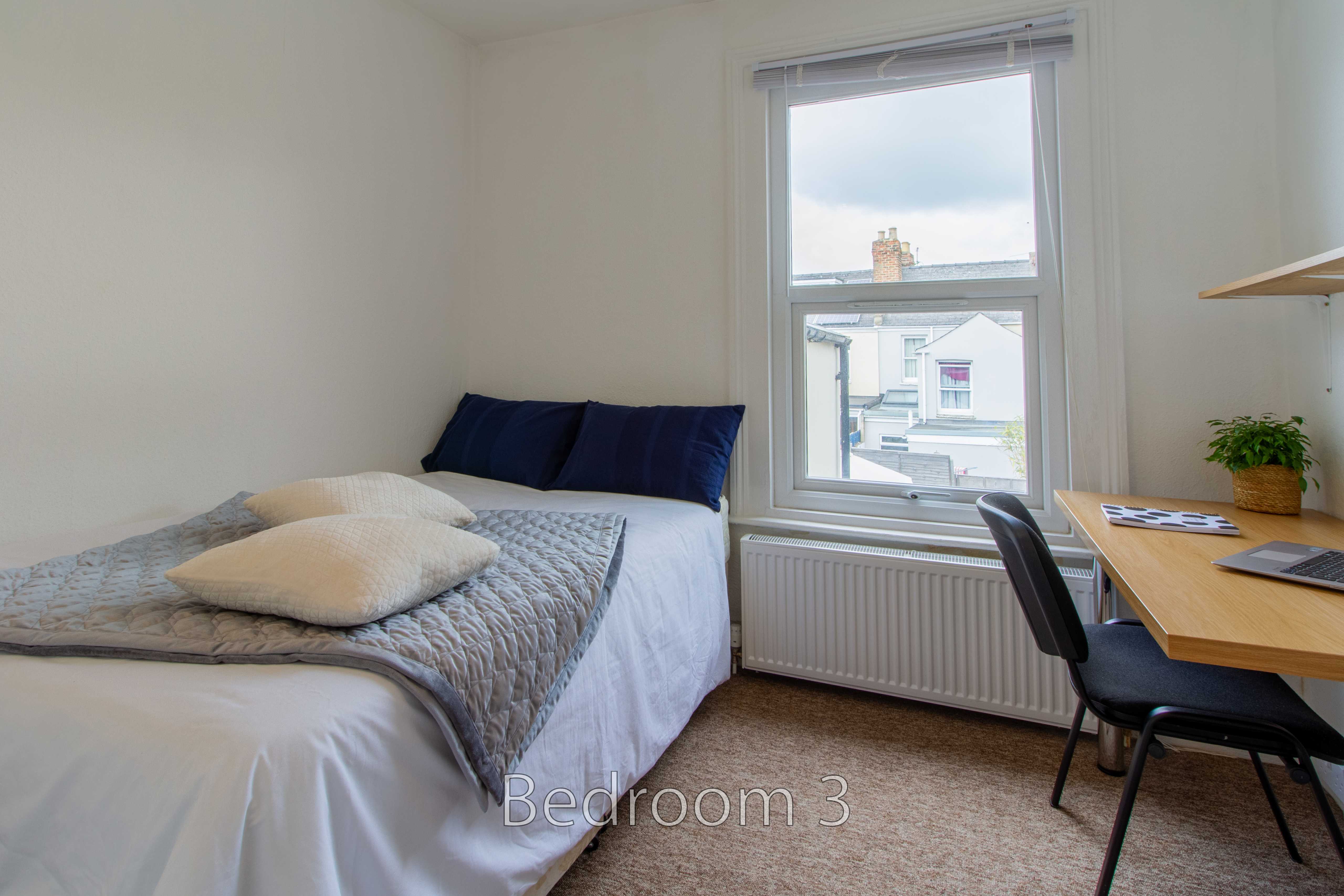A furnished bedroom with a single bed, desk, chair, window and radiator.