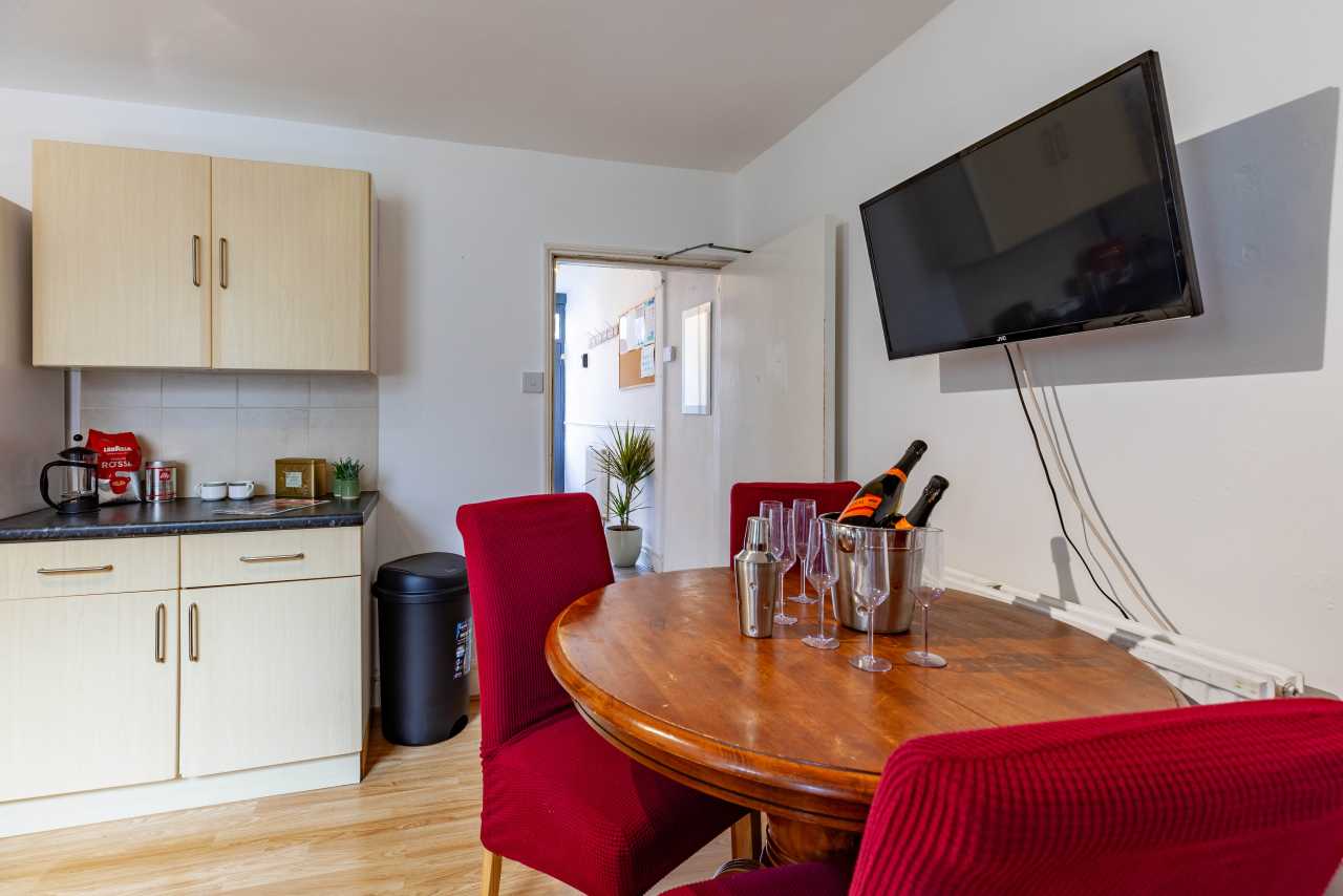 Shared dining and kitchenette area with a wooden table, red chairs, cabinets, sink, television and doorway.