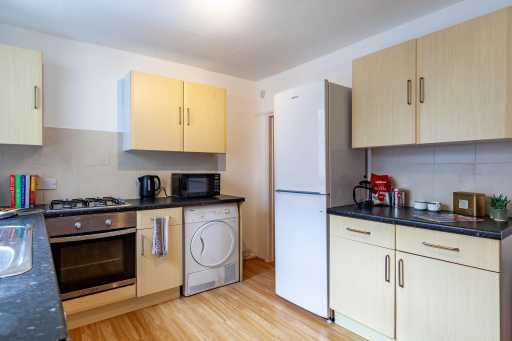Bright fitted kitchen with wood-effect cabinets, cooker, washing machine, refrigerator, kettle and countertop appliances.
