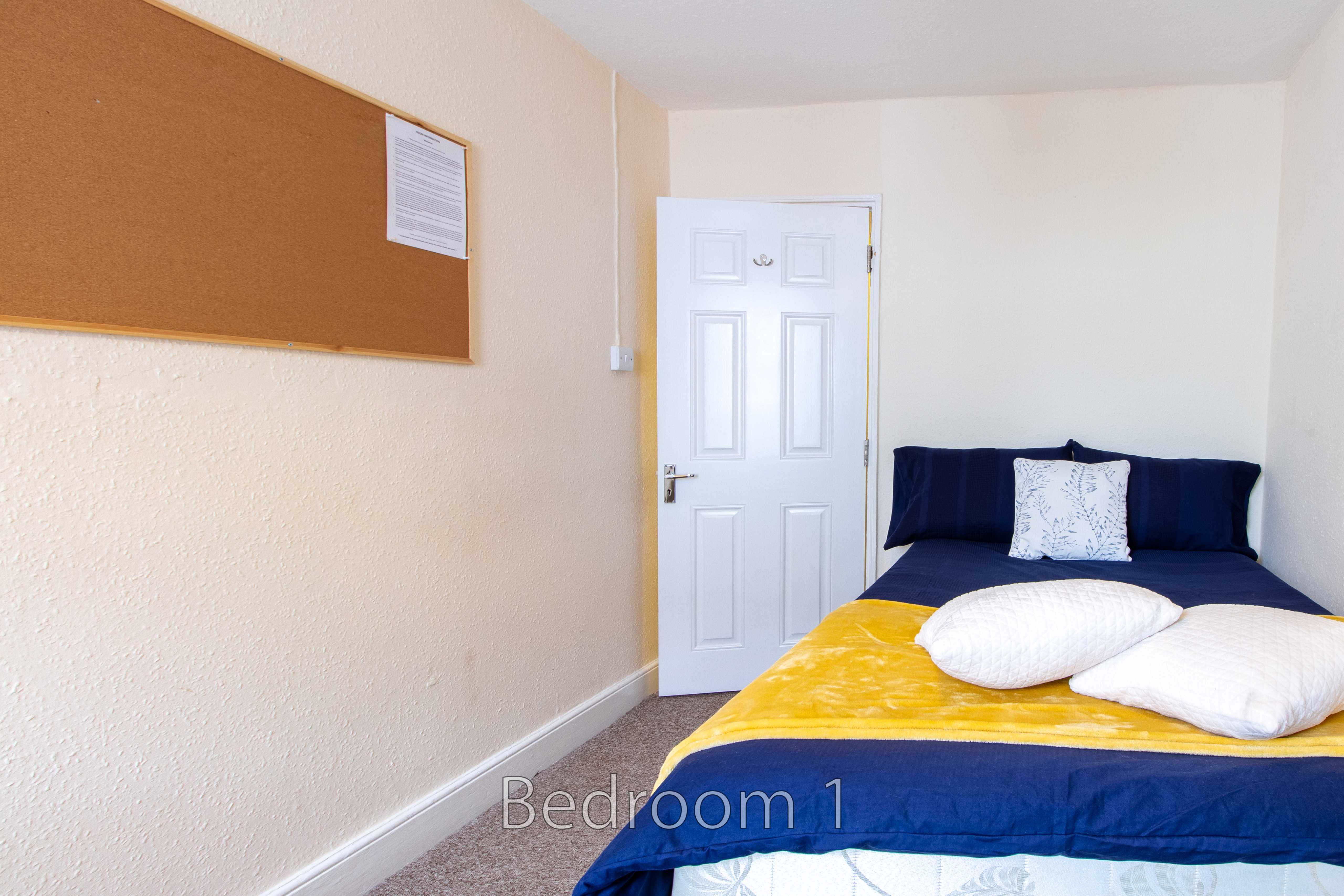 A bedroom with a bed, pillows, a white door and a cork noticeboard.