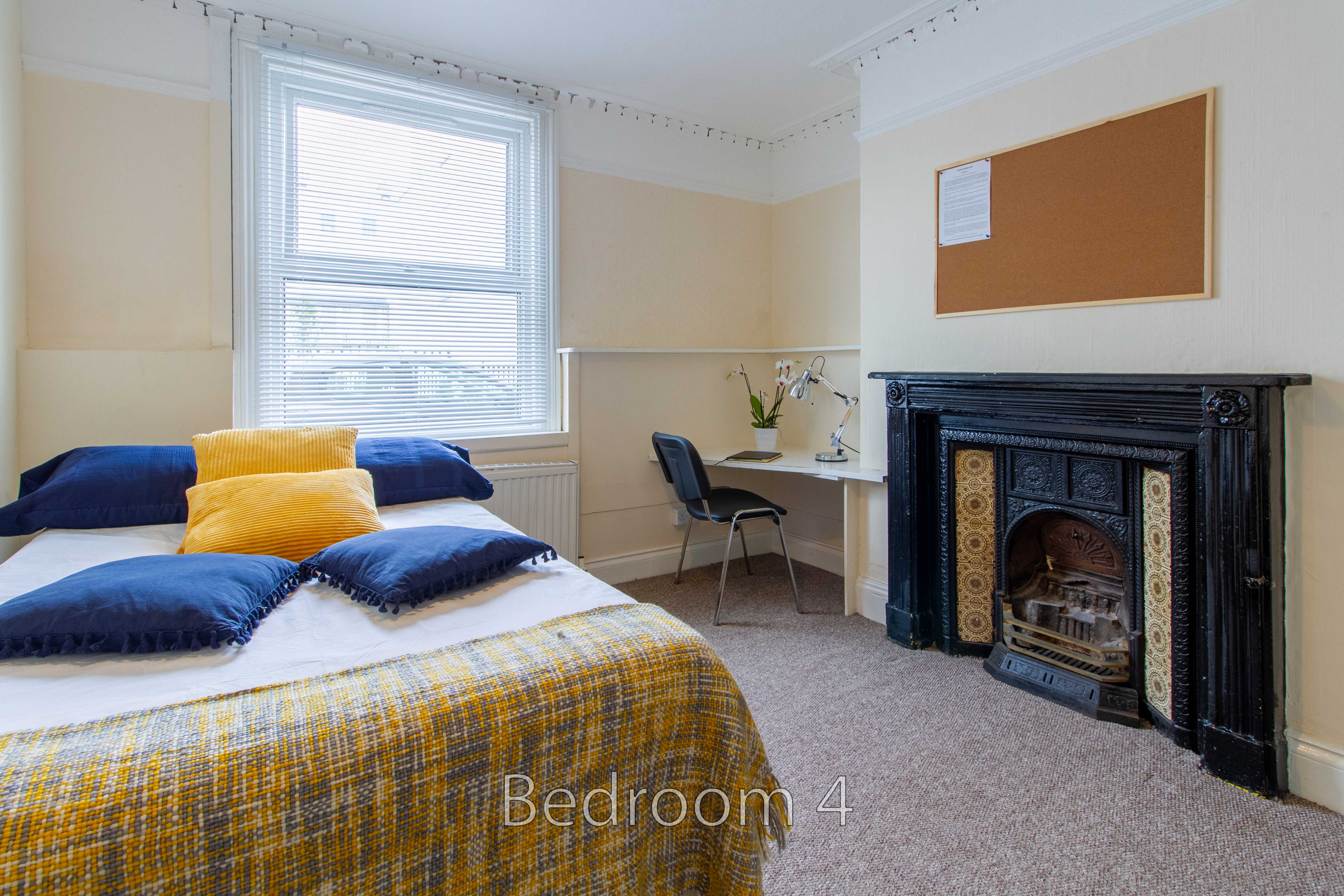 A bedroom with a double bed, desk, window and ornate fireplace.