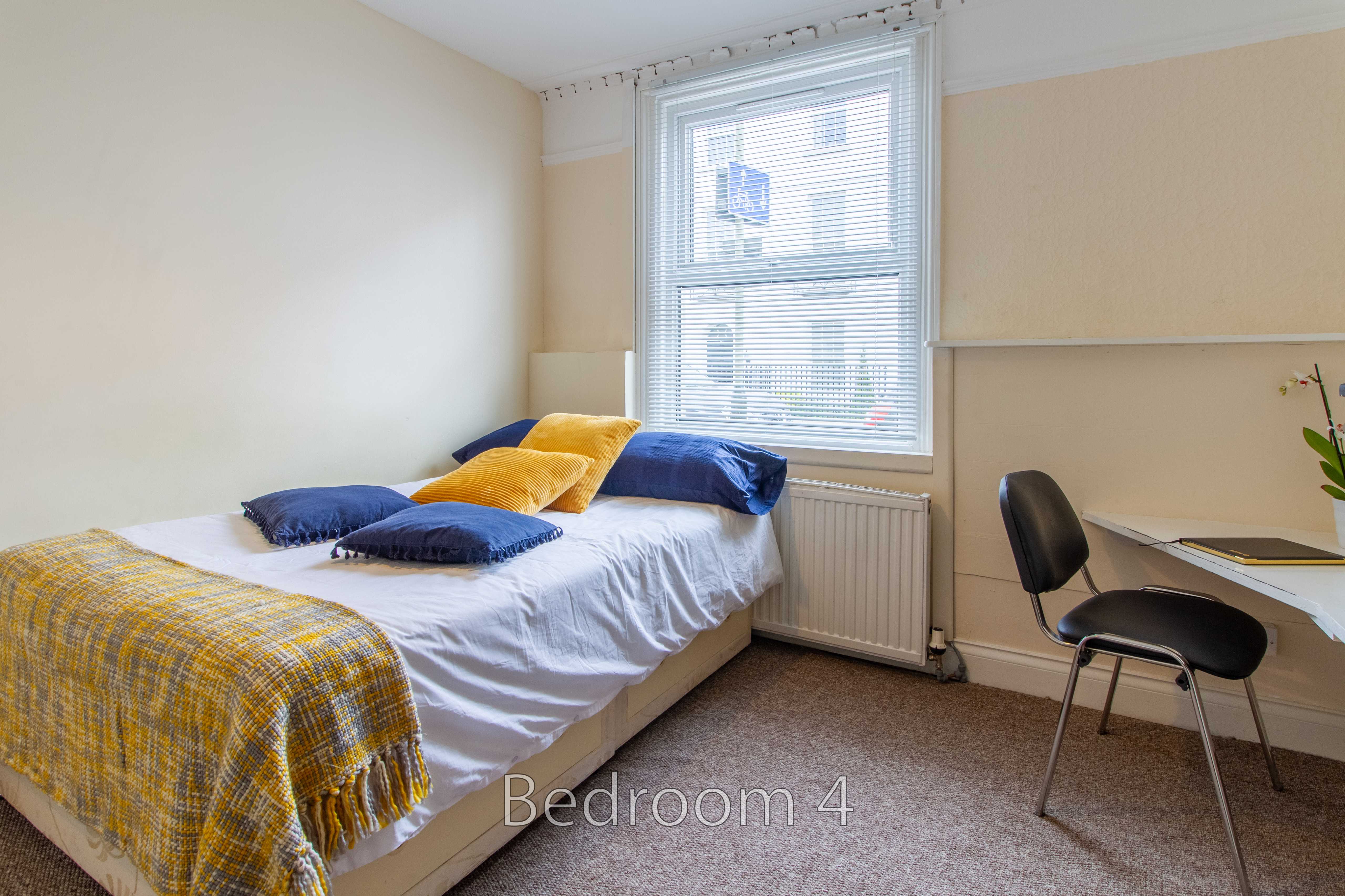 A furnished bedroom with a single bed, window, radiator, desk and chair.