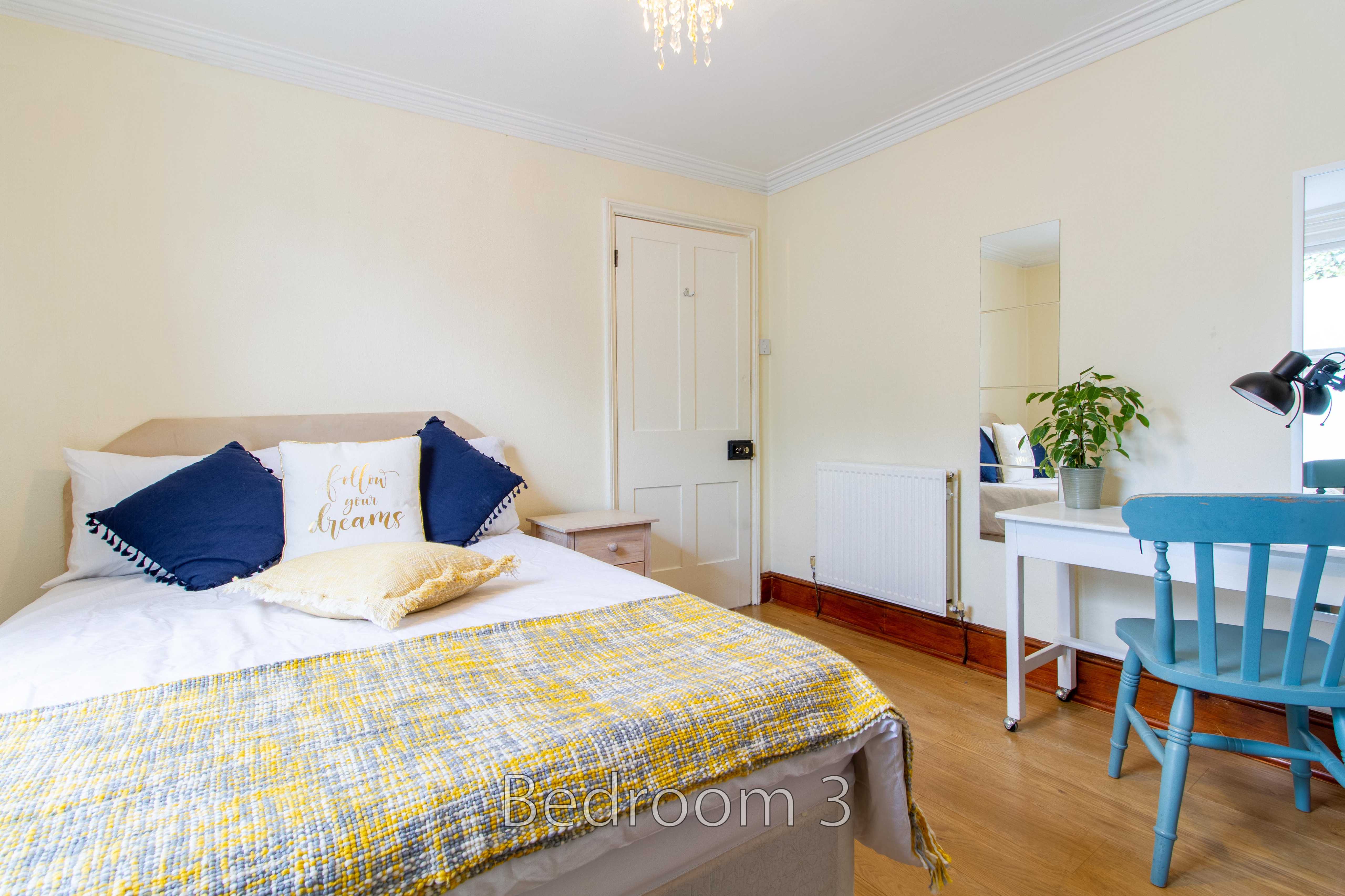 A furnished bedroom with a bed, desk and chair, radiator, and wooden flooring.