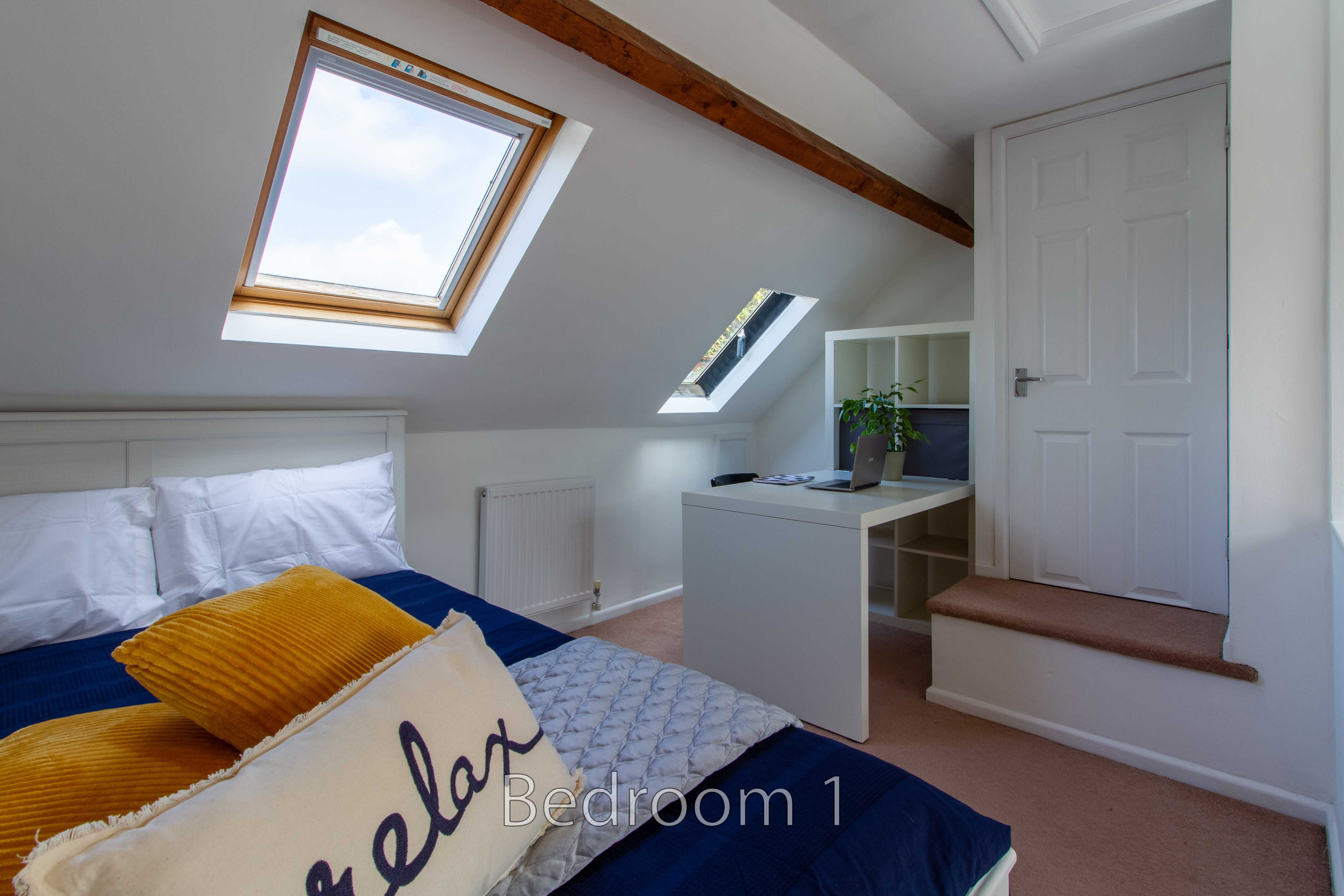 A furnished attic bedroom with a bed, skylights, desk, radiator and white door.