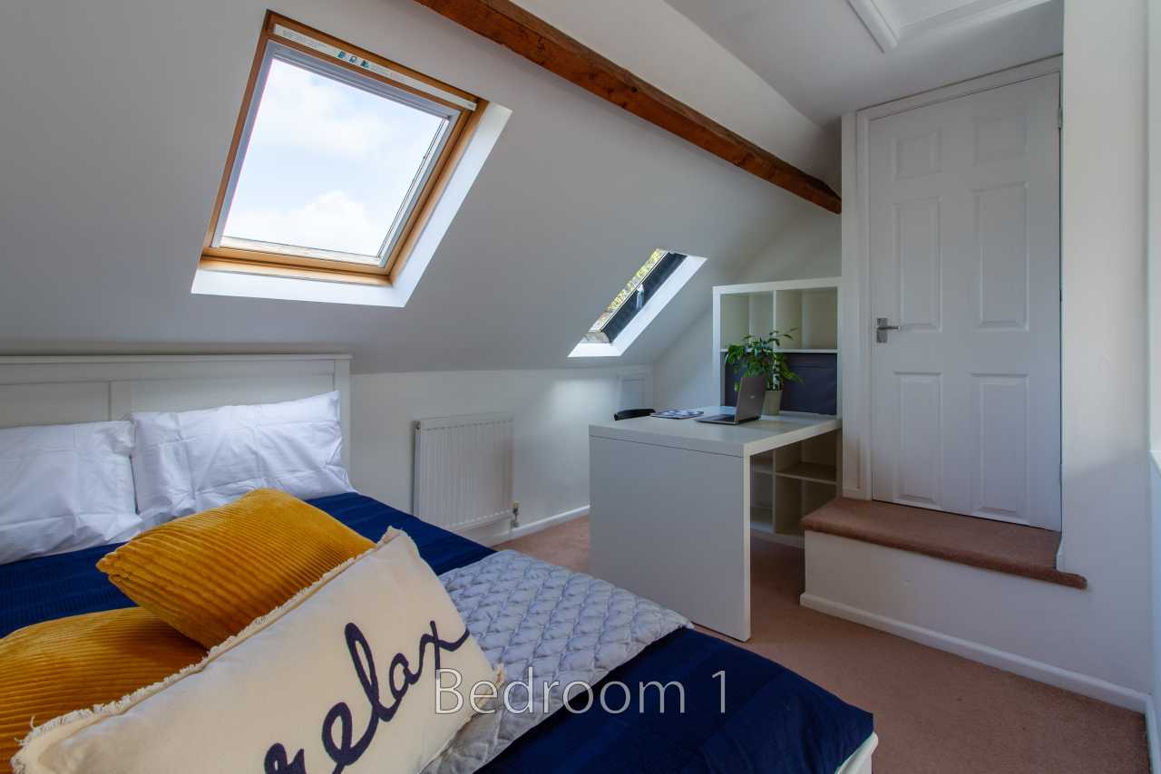 A furnished attic bedroom with a bed, skylights, desk, radiator and white door.