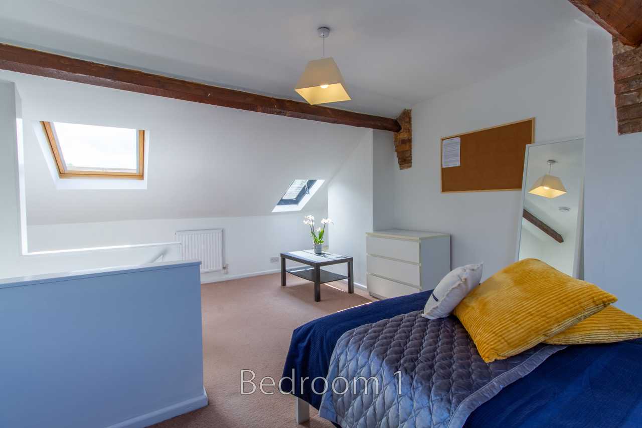 A furnished bedroom with a bed, skylights, exposed wooden beams, a dresser, and a small table.