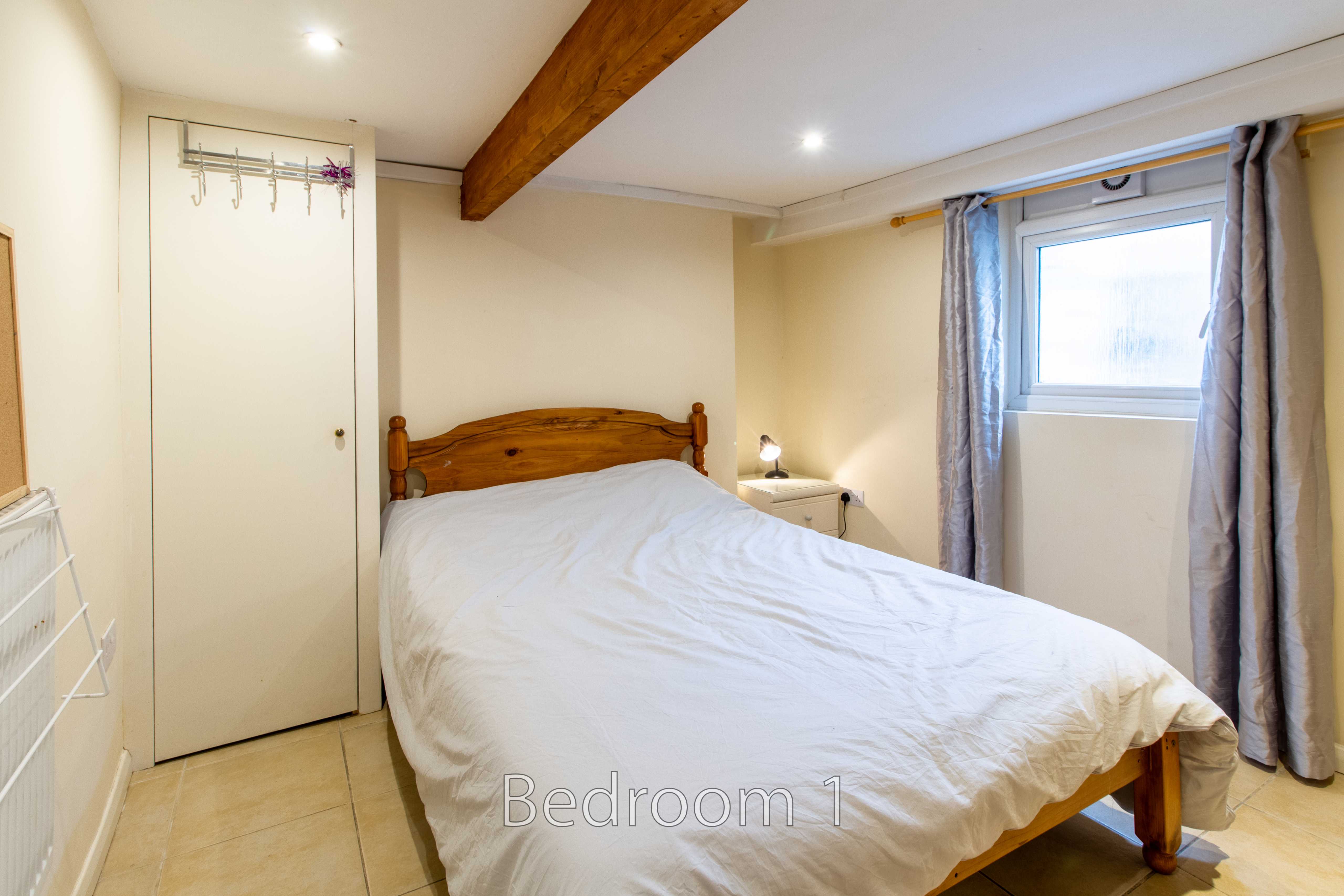 A bedroom with a double bed, wardrobe, window and curtains.