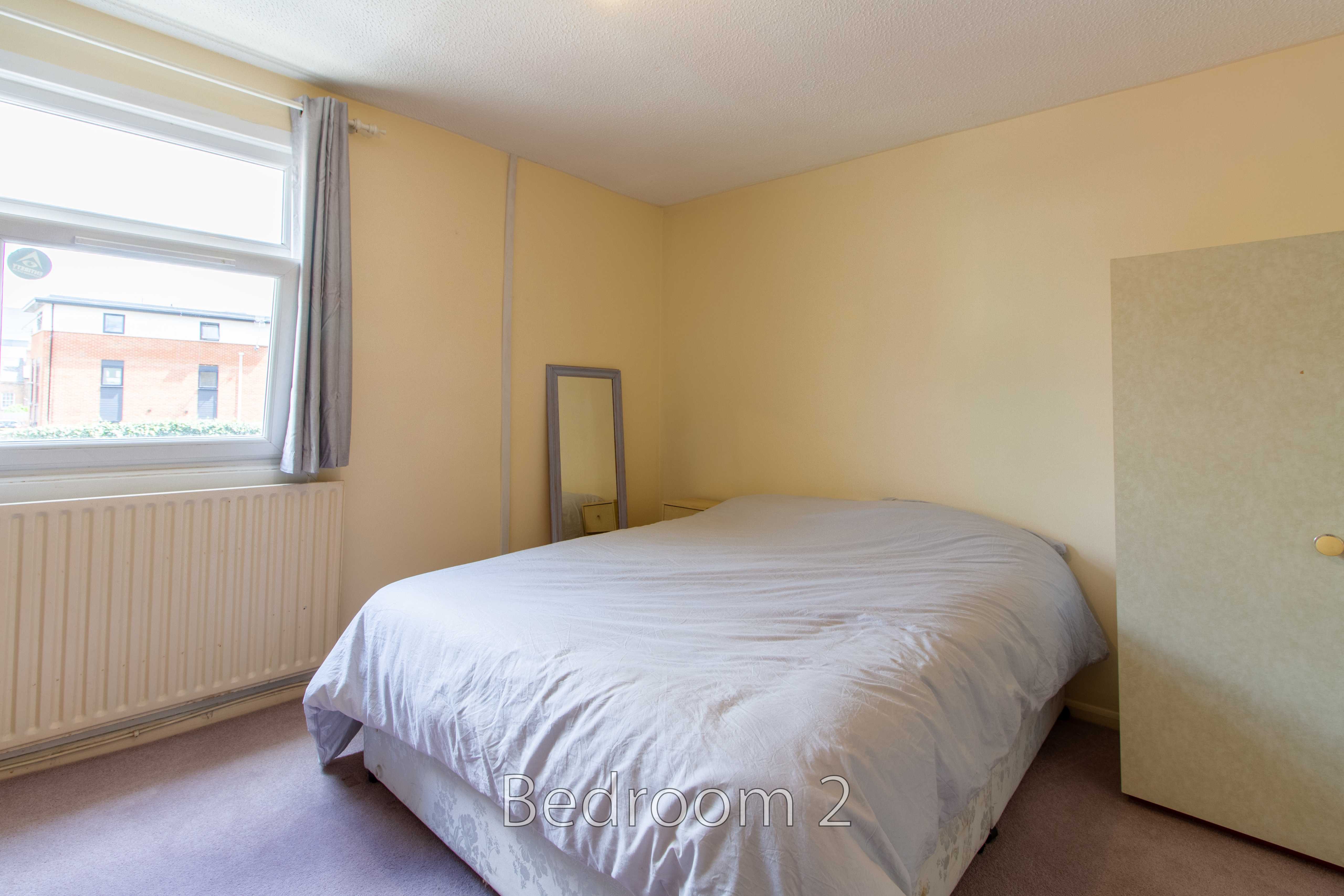A bedroom with a double bed, window, radiator, mirror and wardrobe.