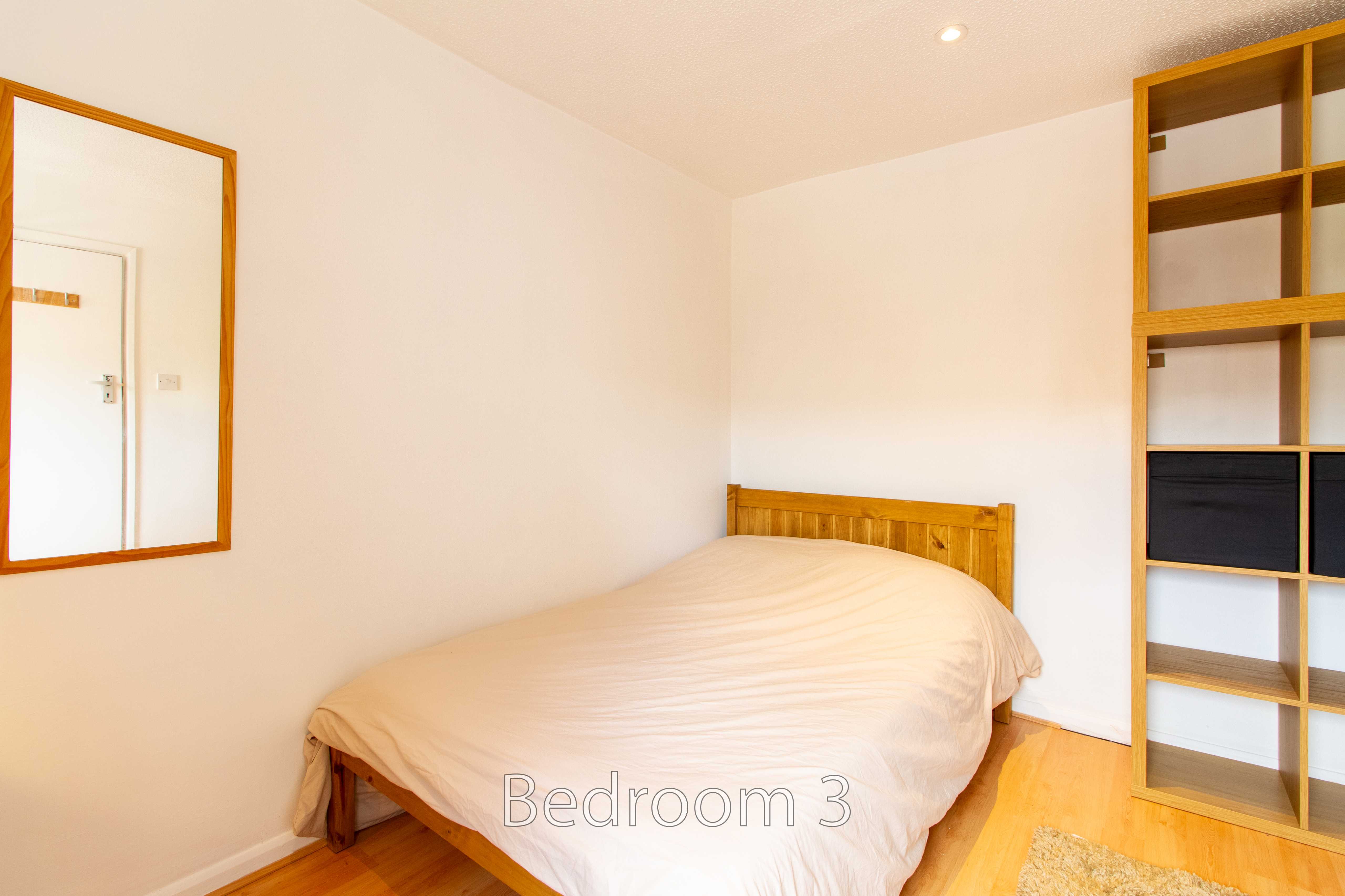 A bedroom with a double bed, wooden floor, wall mirror and open shelving.