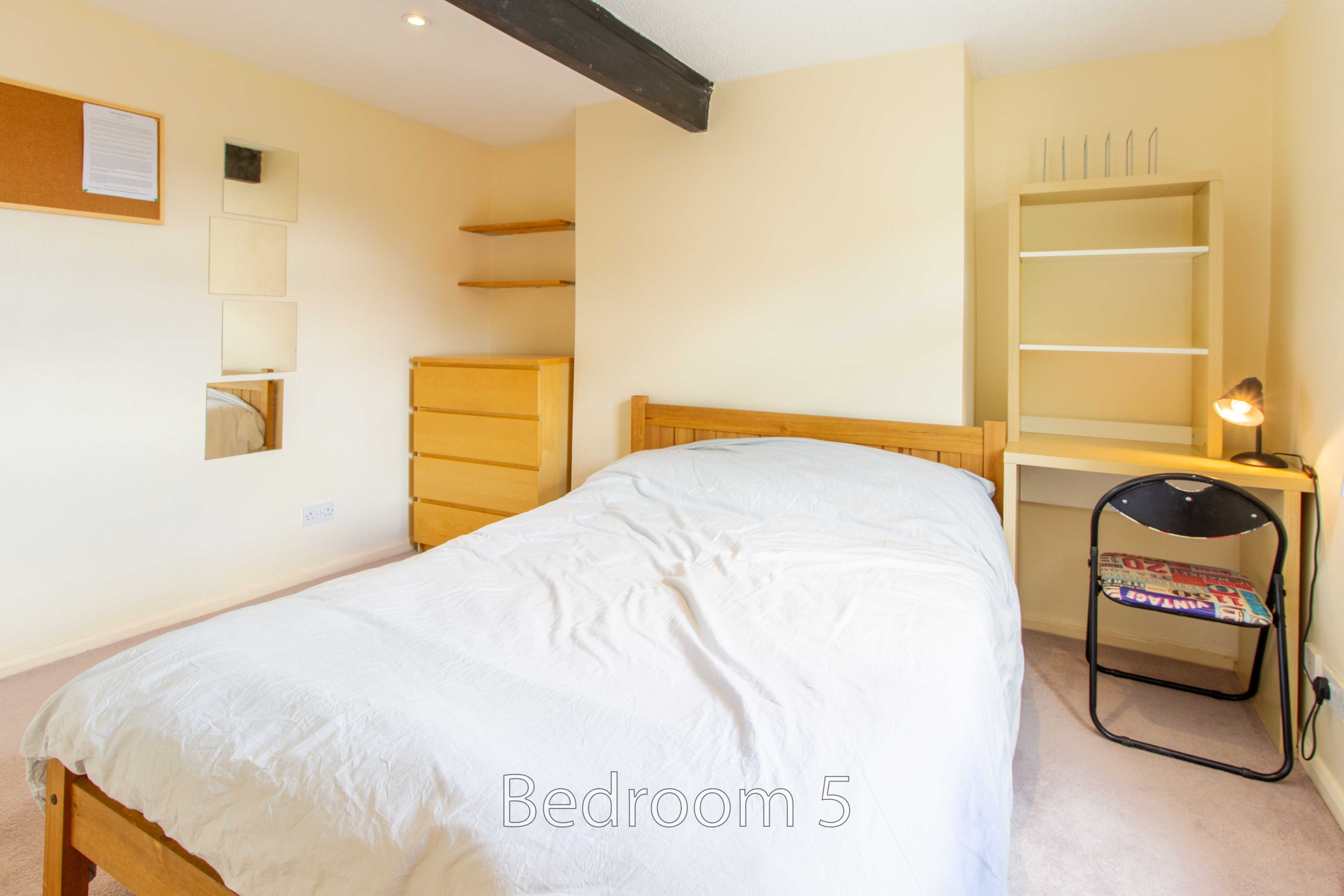 A bedroom with a double bed, wooden furniture, built-in shelving and a folding chair.