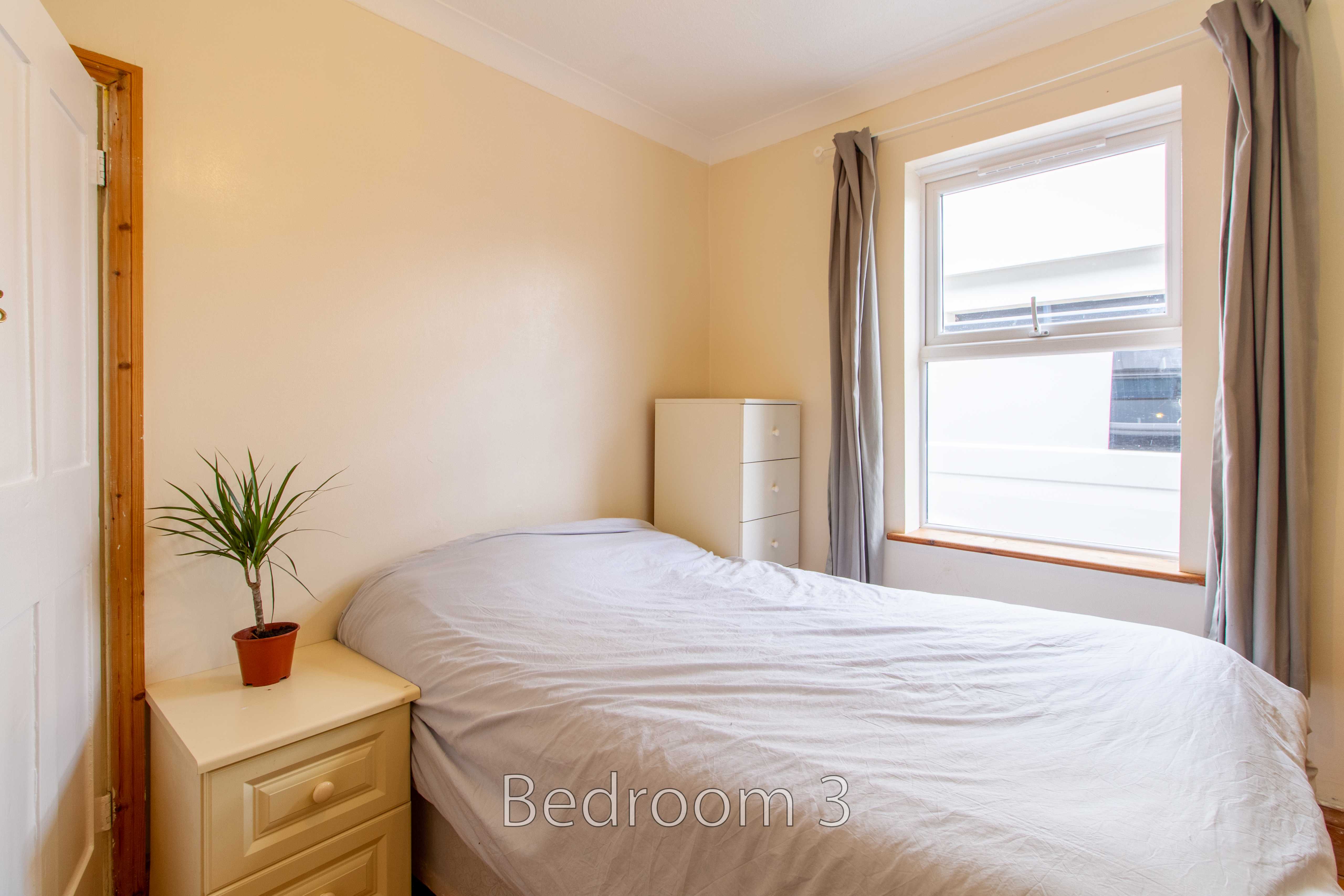 A bedroom with a double bed, bedside table, chest of drawers, curtains and a window.