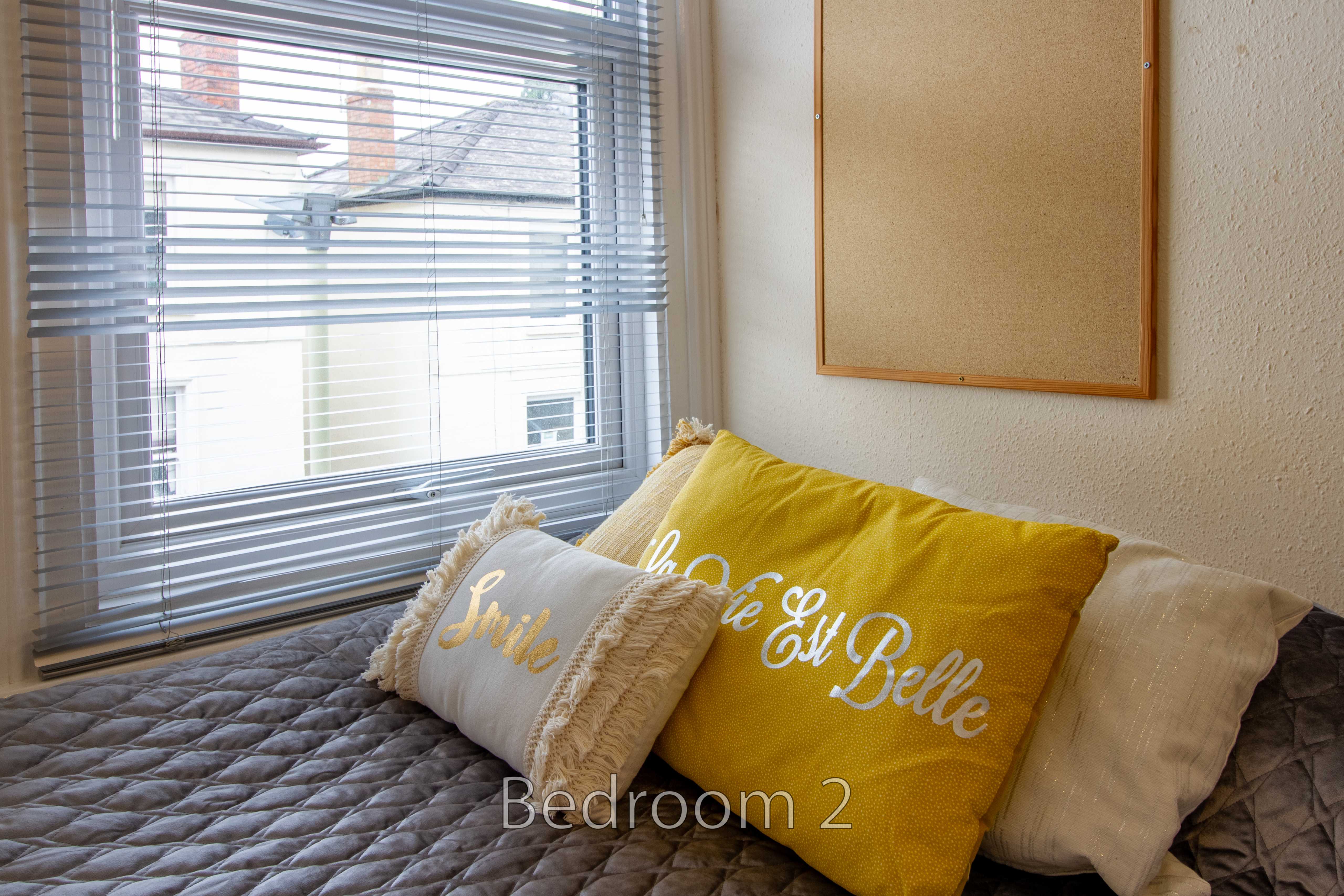 A bedroom with a bed, pillows, a window with blinds, and framed wall art.