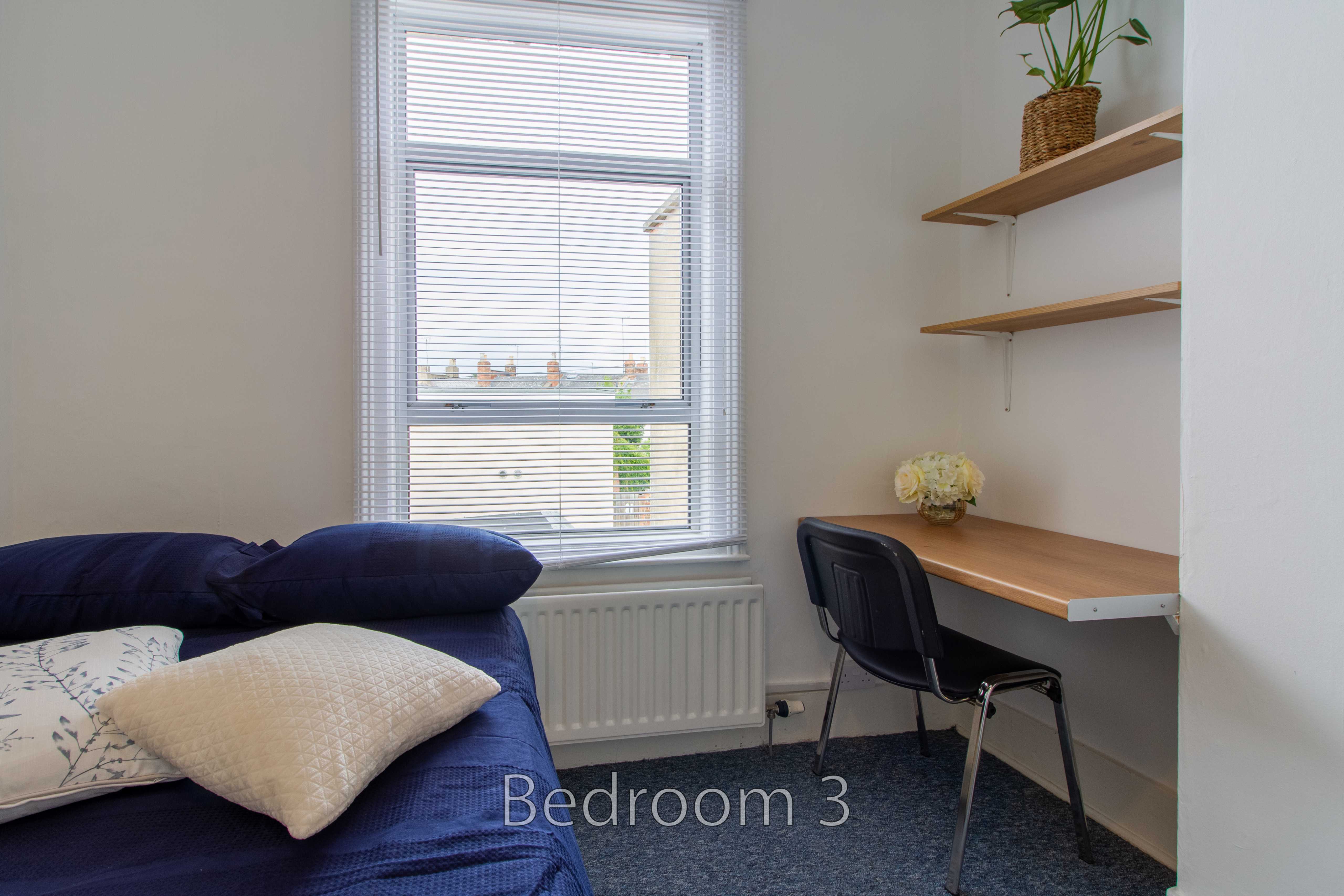 Bedroom with a bed, desk, chair, window and wall shelves.
