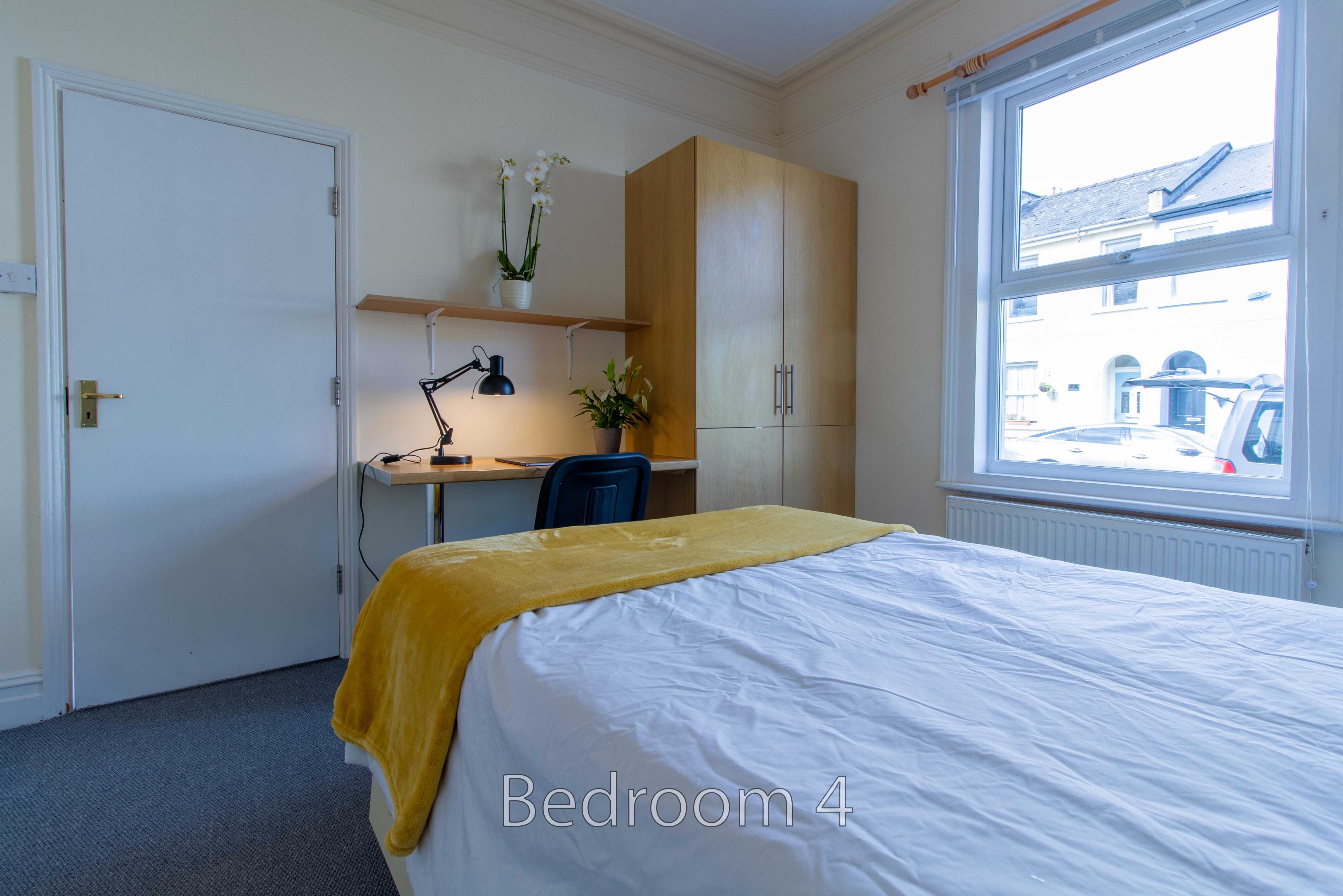 A bedroom with a bed, desk, wardrobe, window and radiator.