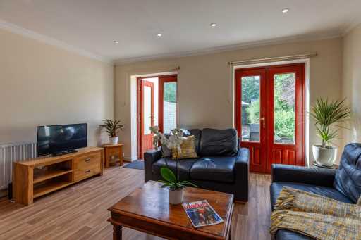 A furnished living room with sofas, a television, a coffee table, plants and glass-panelled doors.