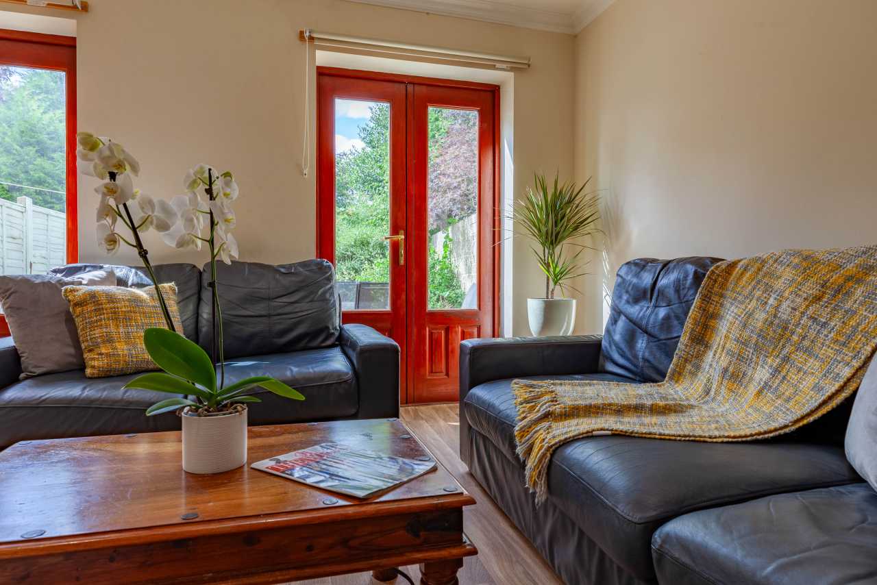 Living room with two sofas, a wooden coffee table, potted plants and glass doors opening to a garden.