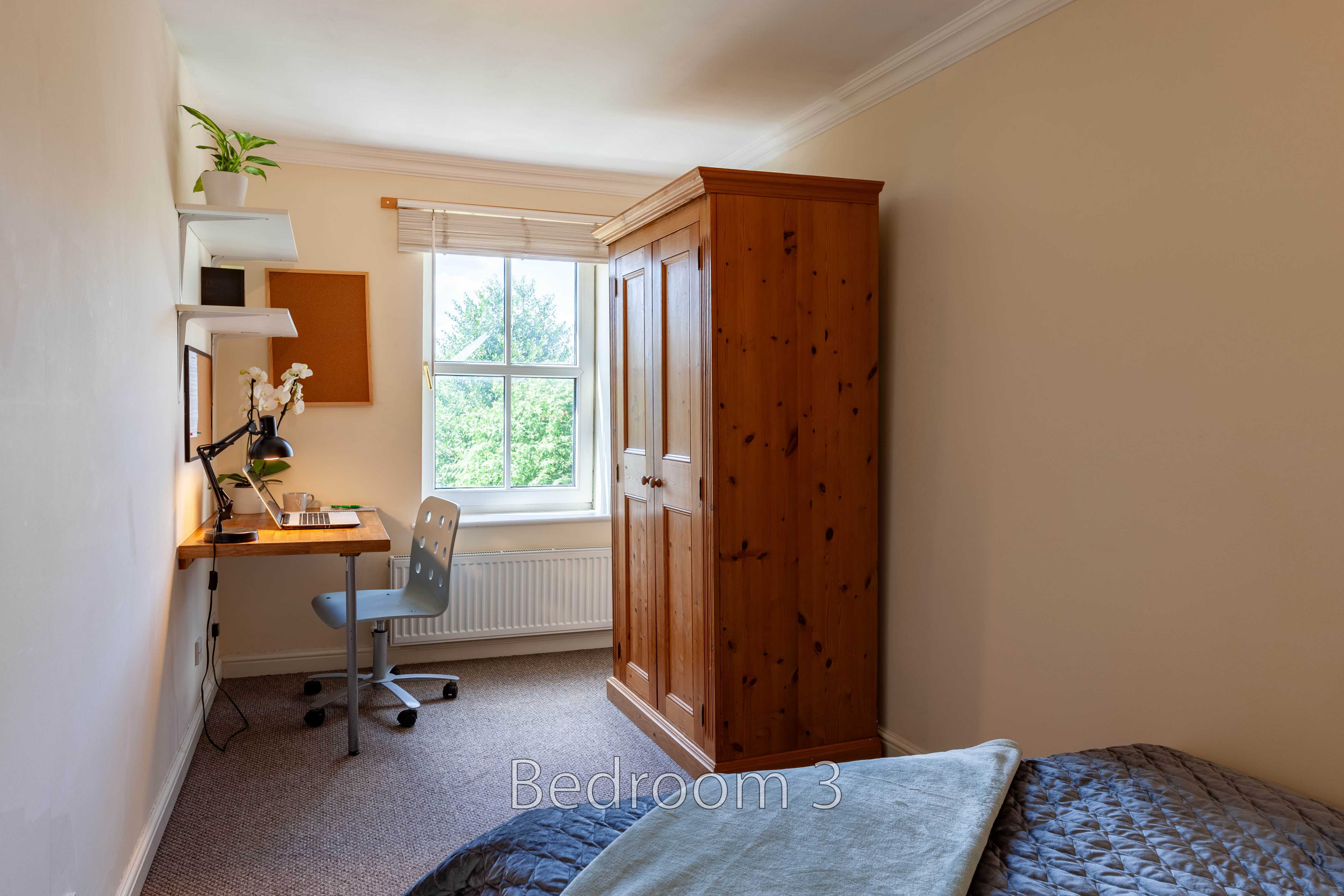 A bedroom with two single beds, a desk and chair, a wardrobe, a window and a radiator.