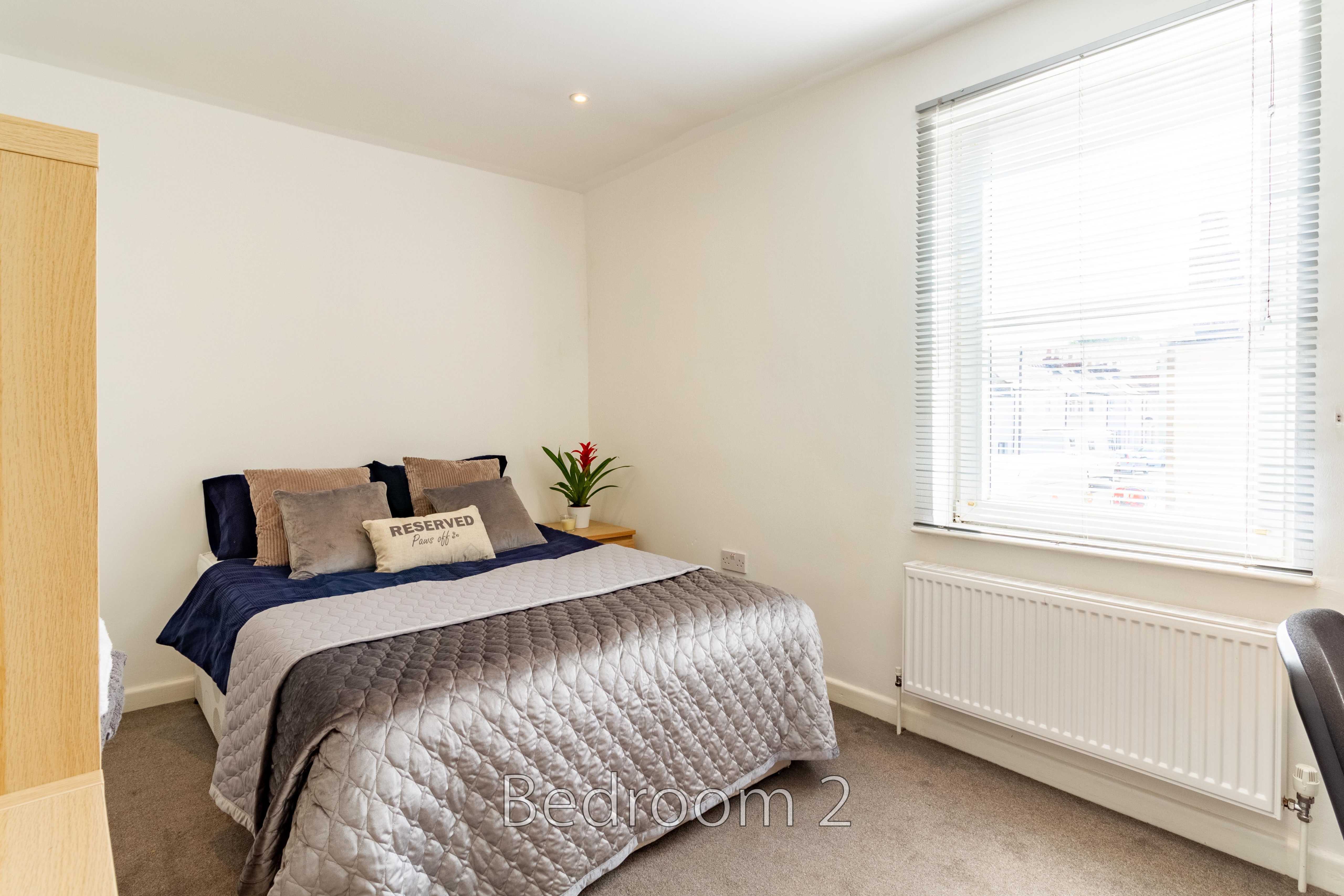 A furnished bedroom with a double bed, bedside table, wardrobe, radiator and window with blinds.