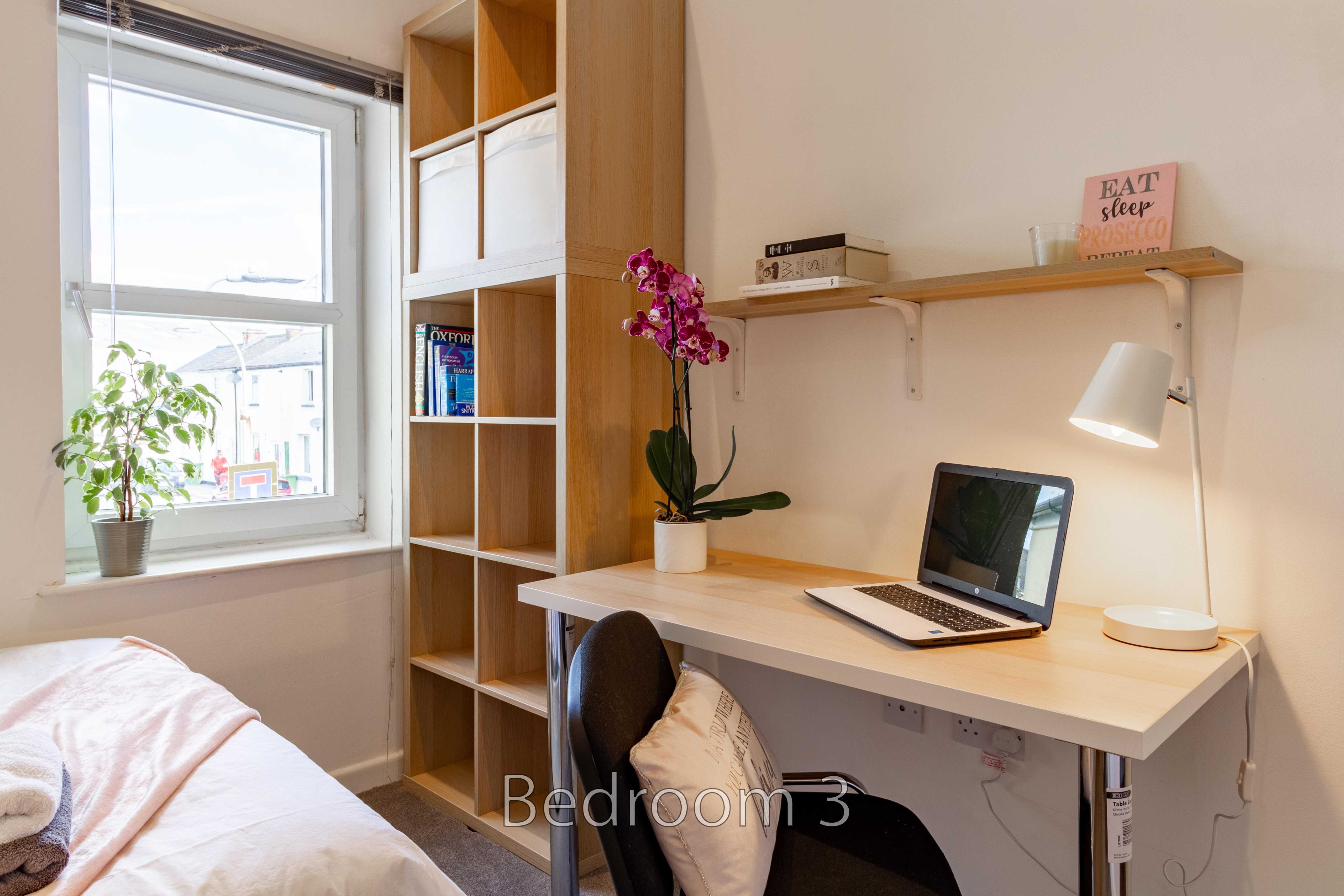 Bedroom with a bed, desk, laptop, shelving, wardrobe and window.