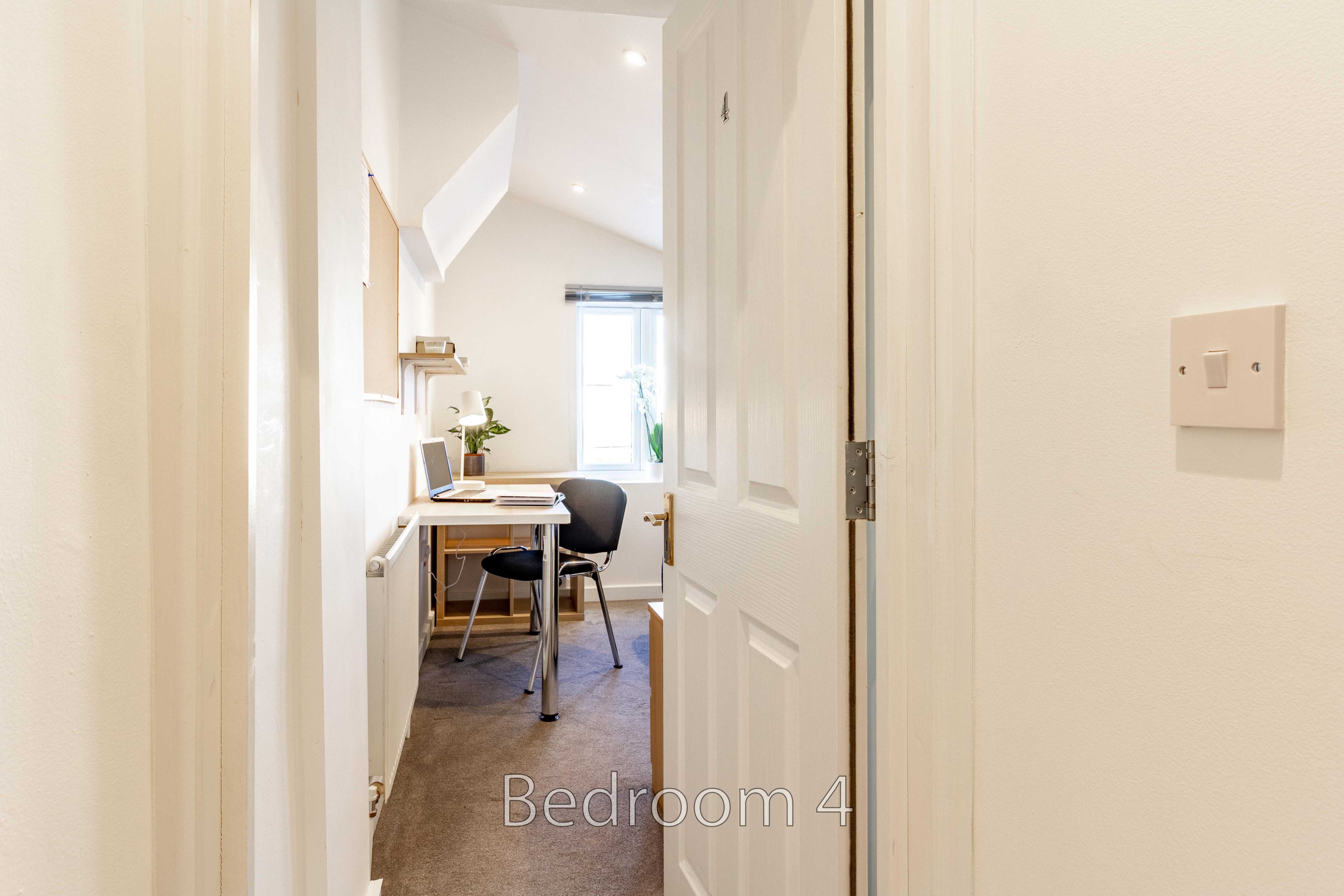 A narrow bedroom with a desk and chair, viewed through an open doorway.
