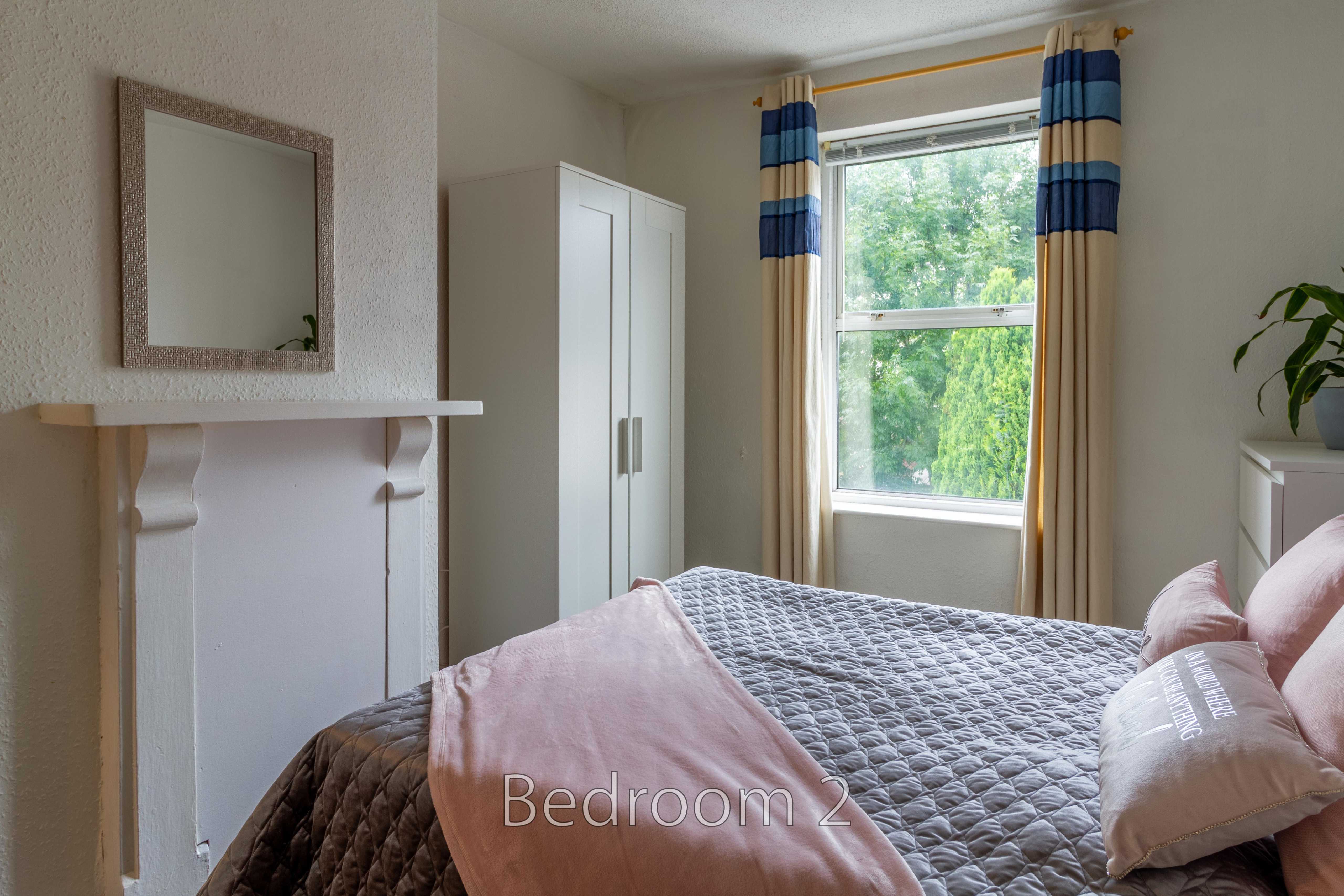 A bedroom with a double bed, wardrobe, window, curtains and a fireplace surround.