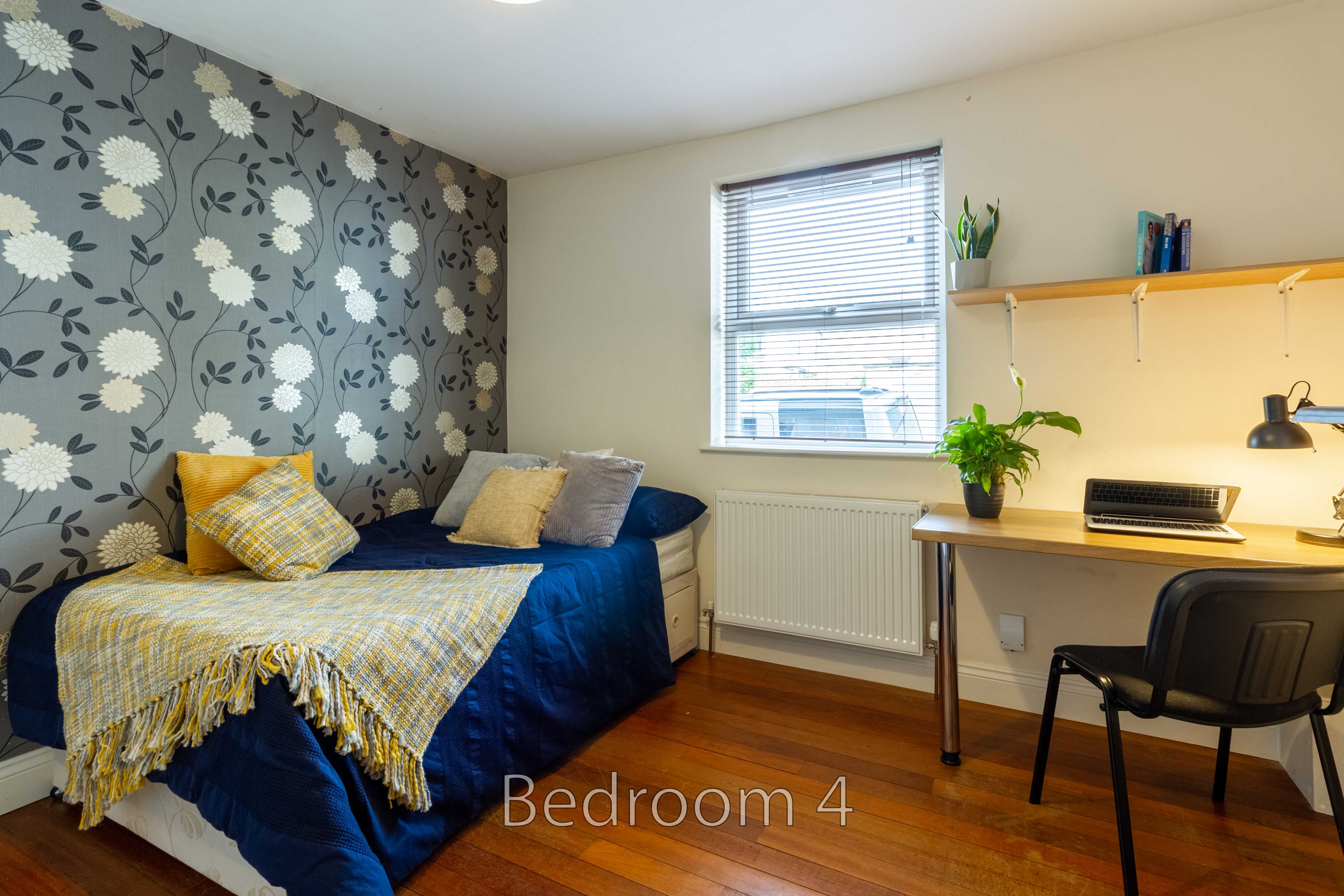 Bedroom with a single bed, desk, chair, window and floral wallpaper.