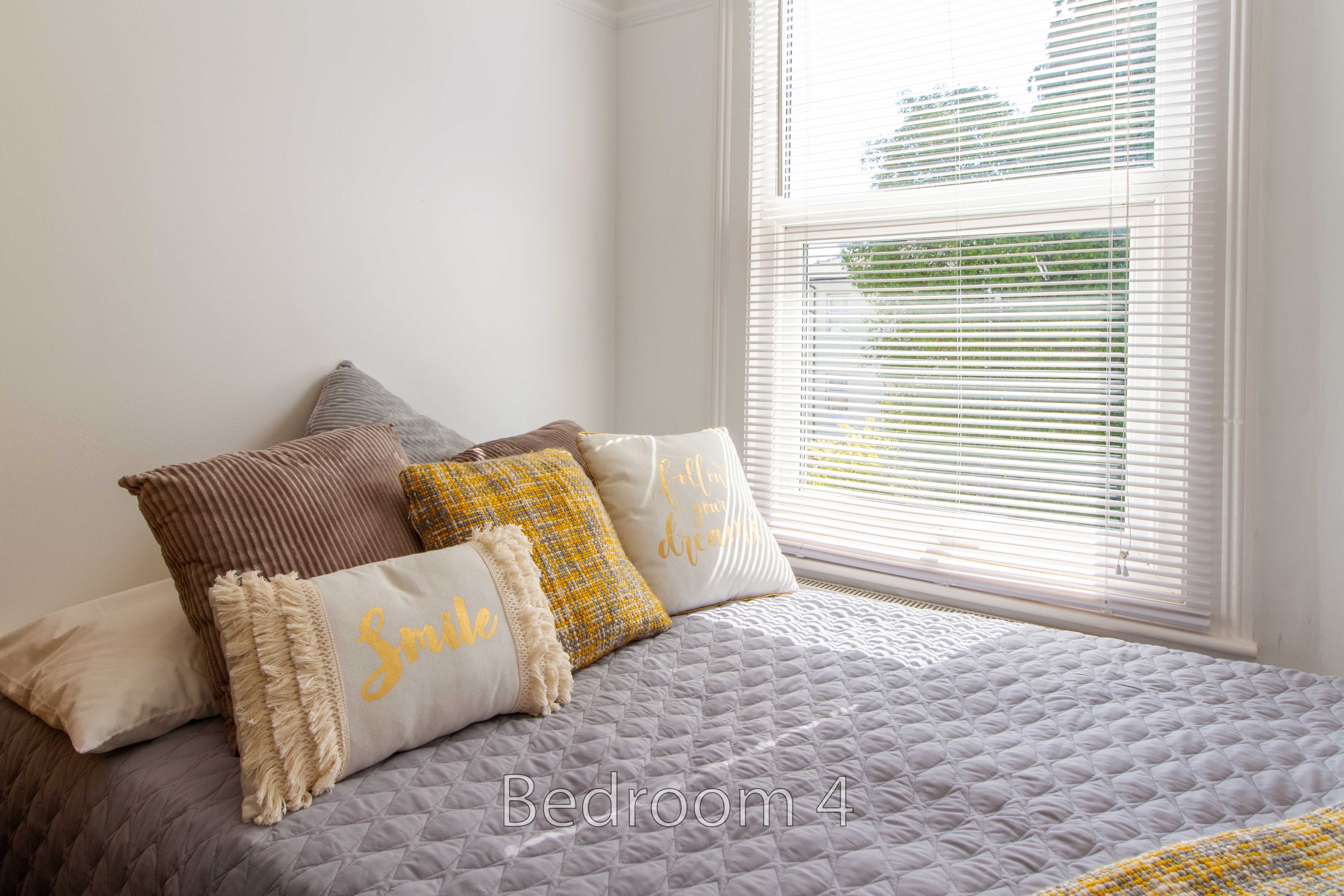 A bedroom with a made bed, decorative pillows and a window with blinds.