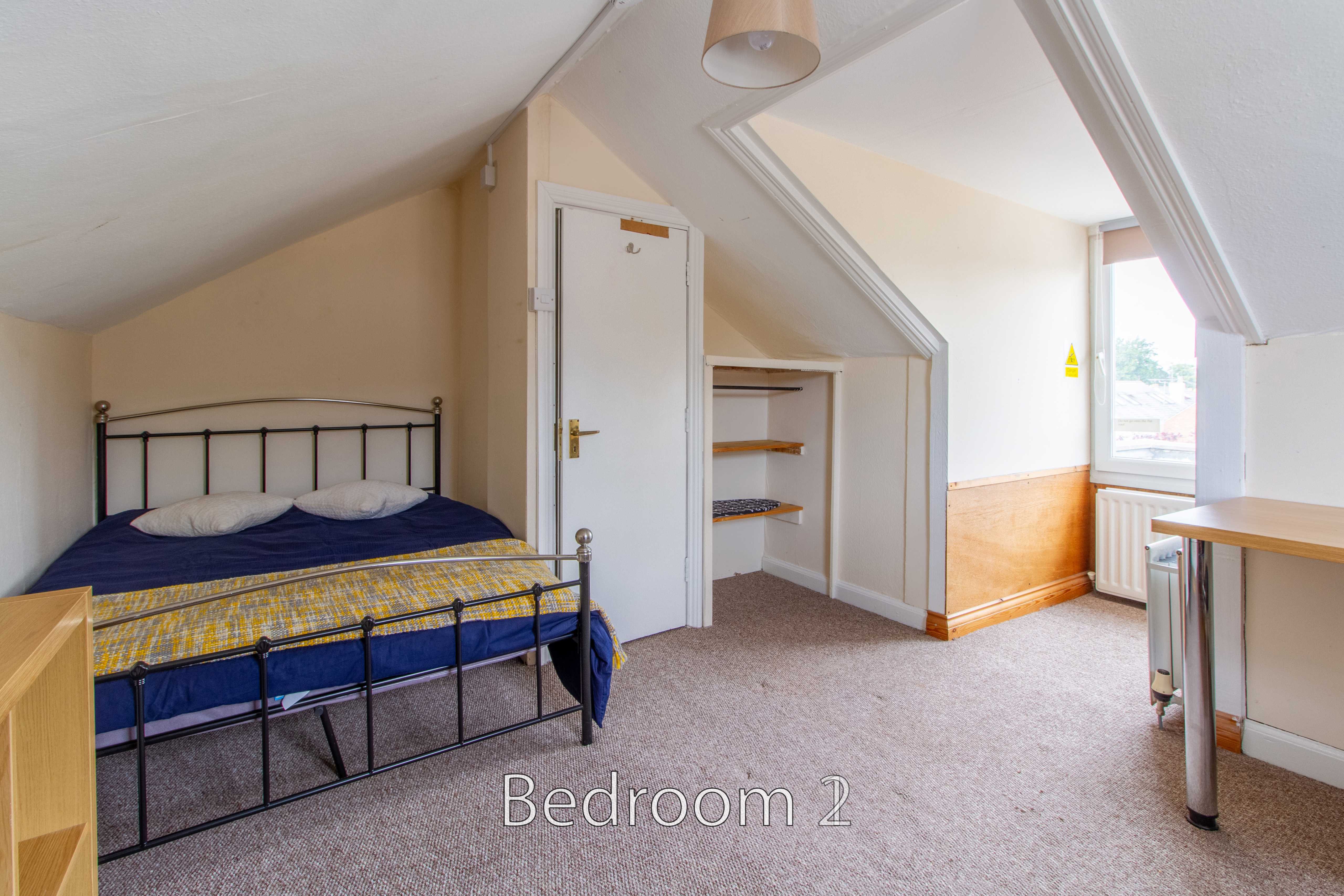 Bedroom with a metal bed, sloped ceiling, built-in shelving, carpeted floor and a window.