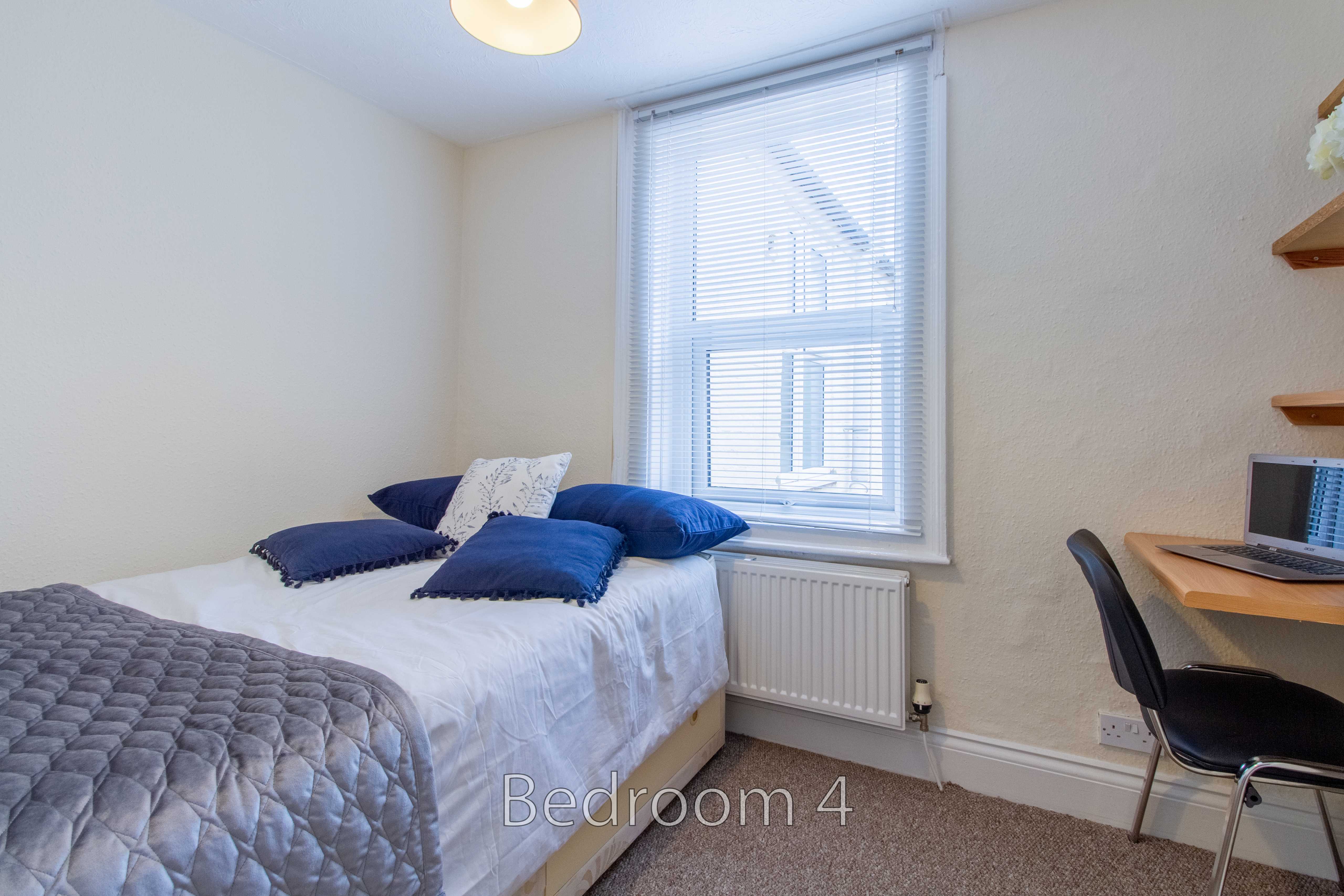 A furnished bedroom with a bed, window, radiator, desk and chair.