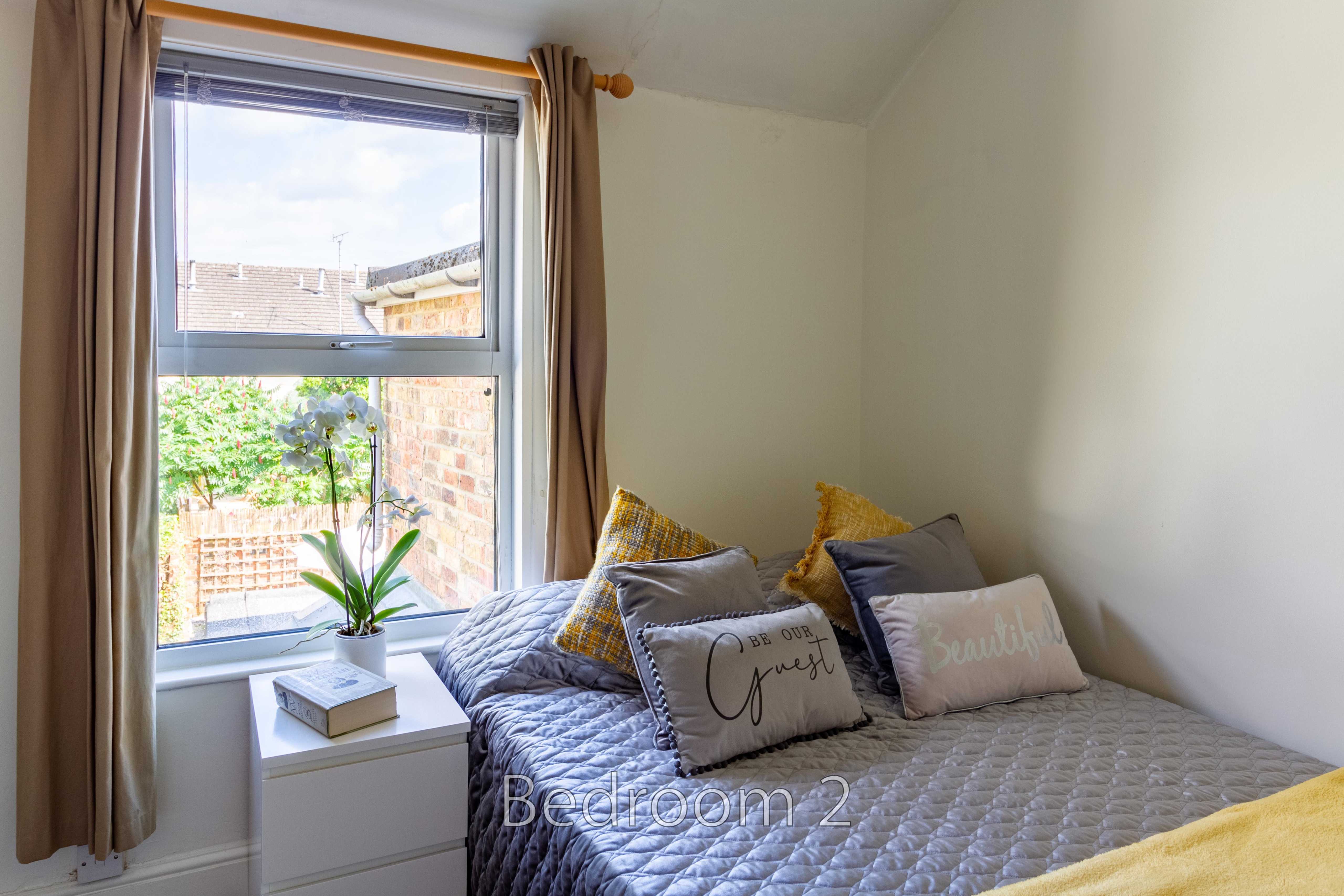 A bedroom with a double bed, quilted cover, pillows, bedside drawers, window and curtains.