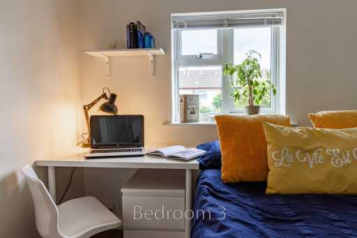 Bedroom with a bed, desk, laptop, chair, shelf and window.