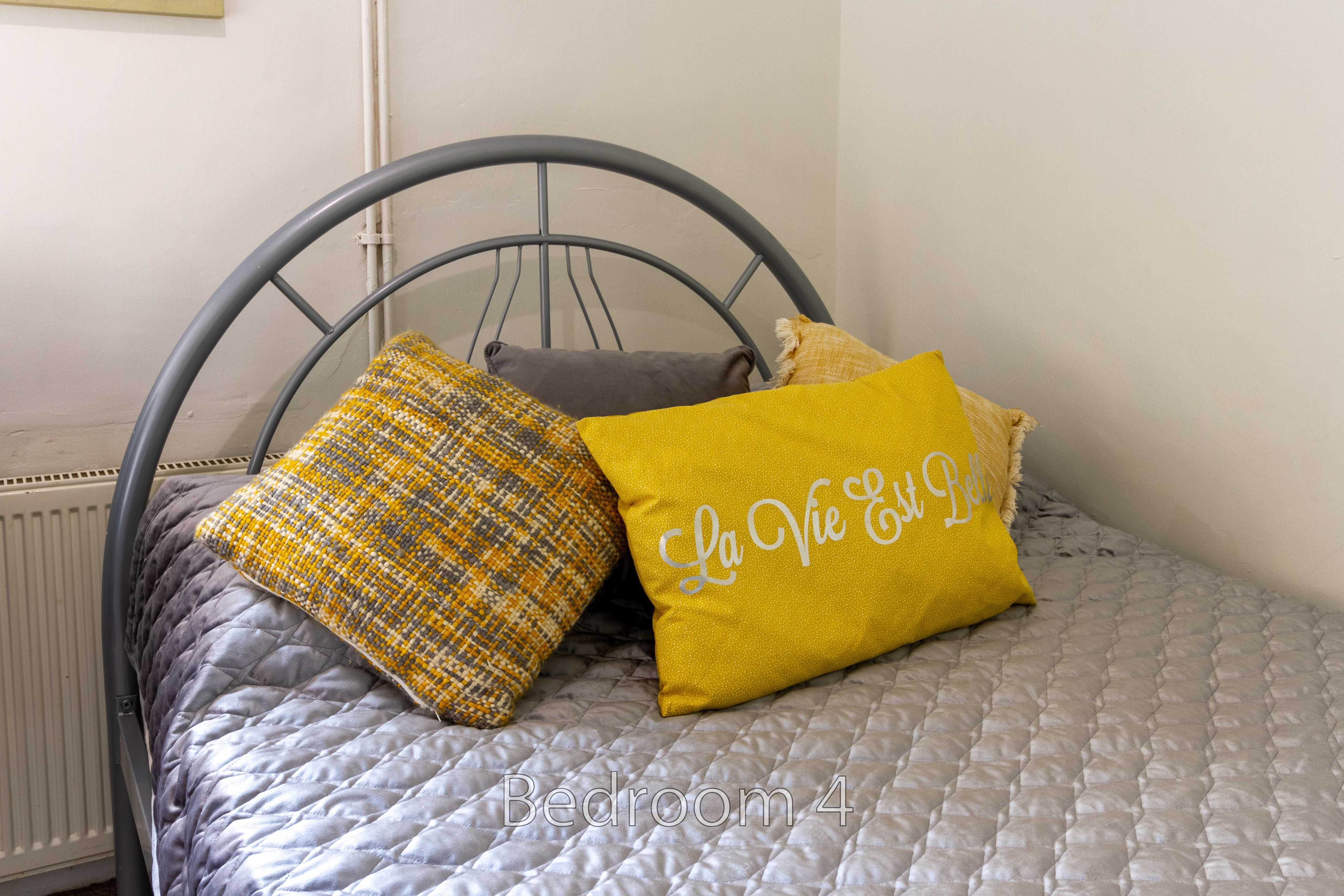 A bed with a grey quilted cover and yellow and grey cushions in a bedroom.