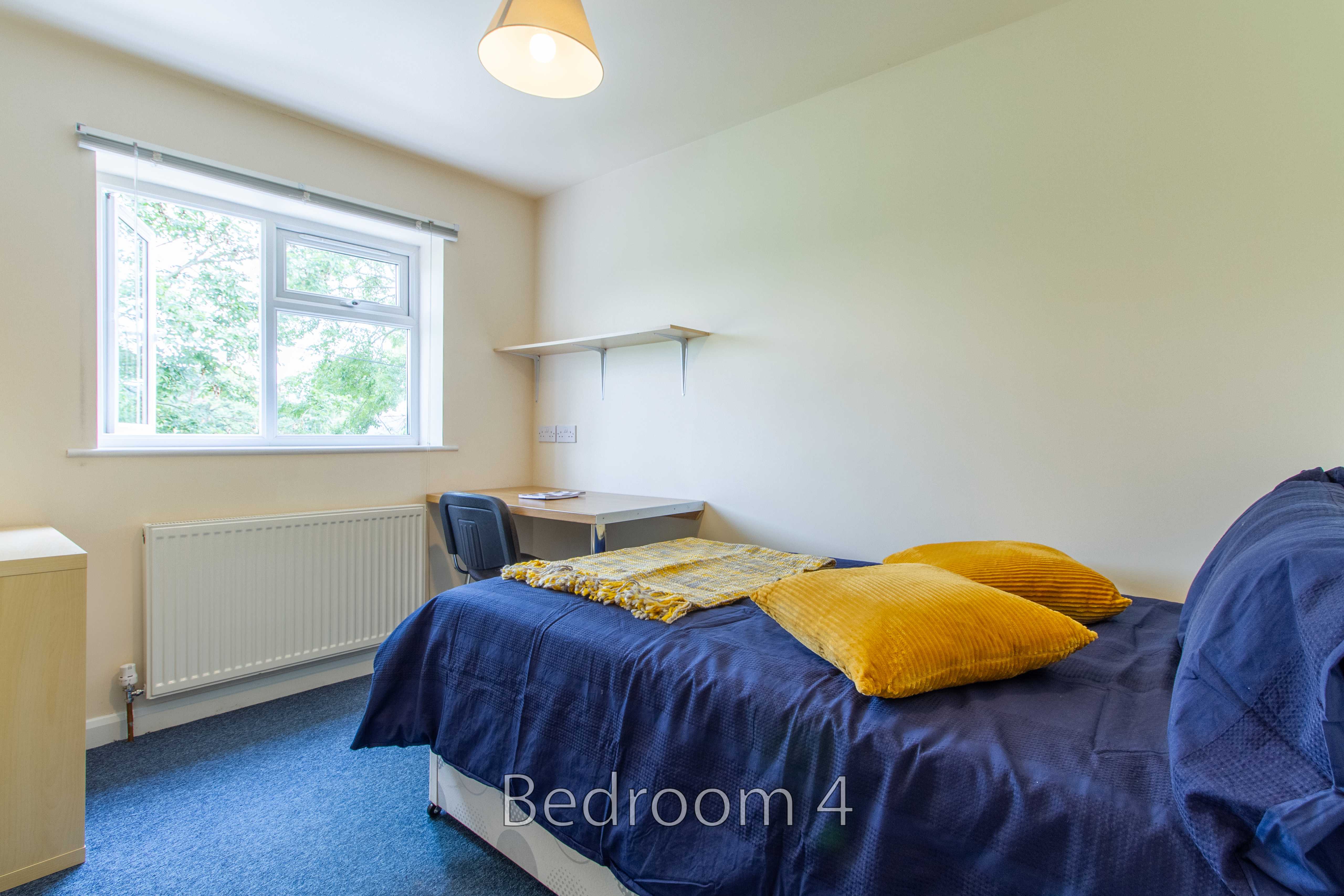 A furnished bedroom with a double bed, desk, shelves, radiator and window.