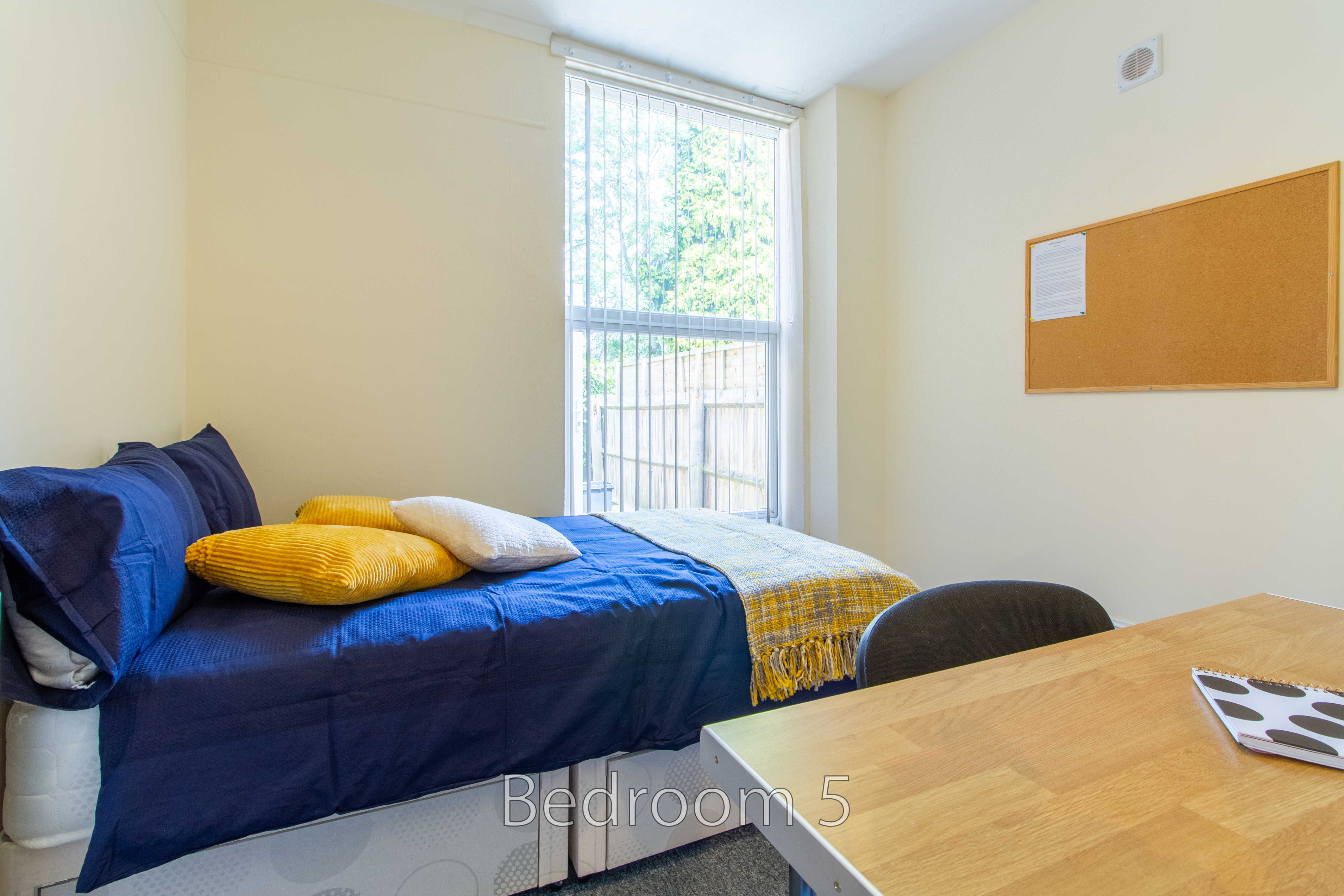 Bedroom with a single bed, desk, chair, window and wall-mounted noticeboard.