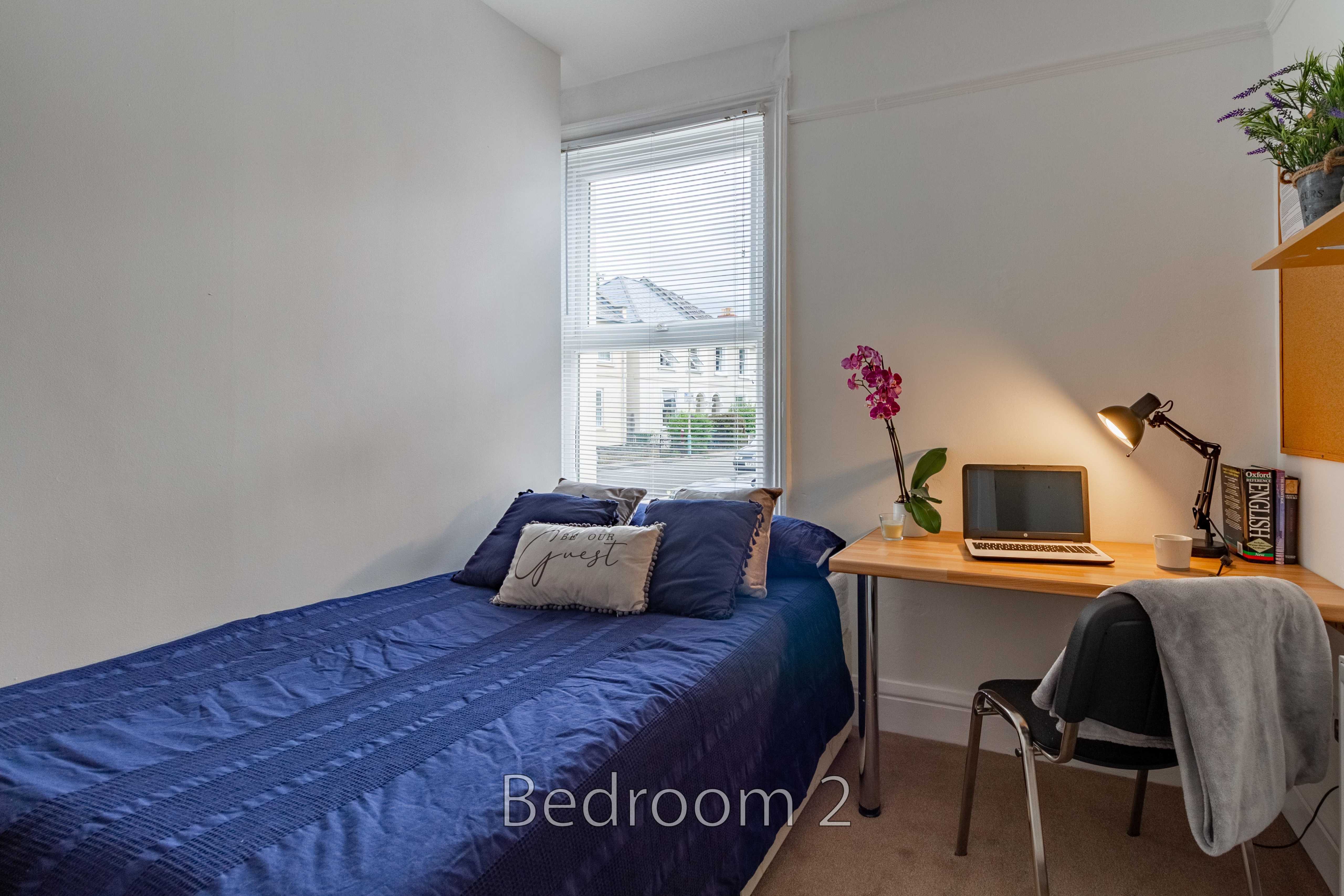 A furnished bedroom with a single bed, desk, chair, window and wardrobe.