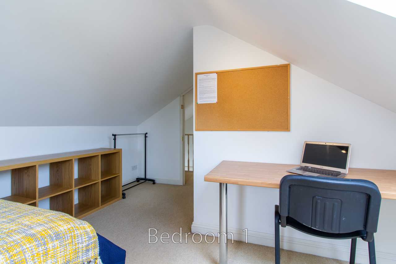A furnished attic bedroom with a single bed, shelving, desk, chair and laptop.