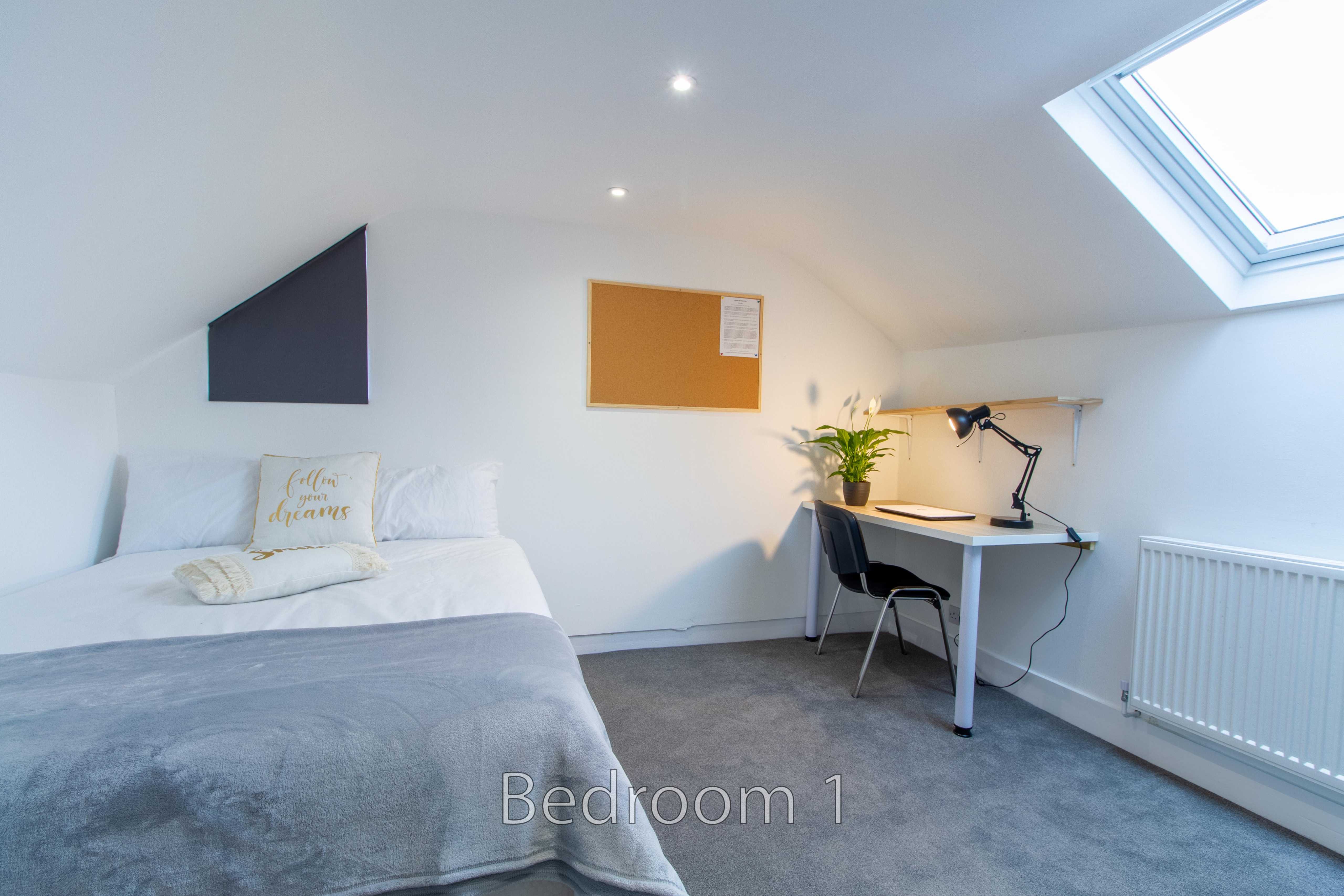 A bright attic bedroom with a bed, desk, chair, skylight and radiator.
