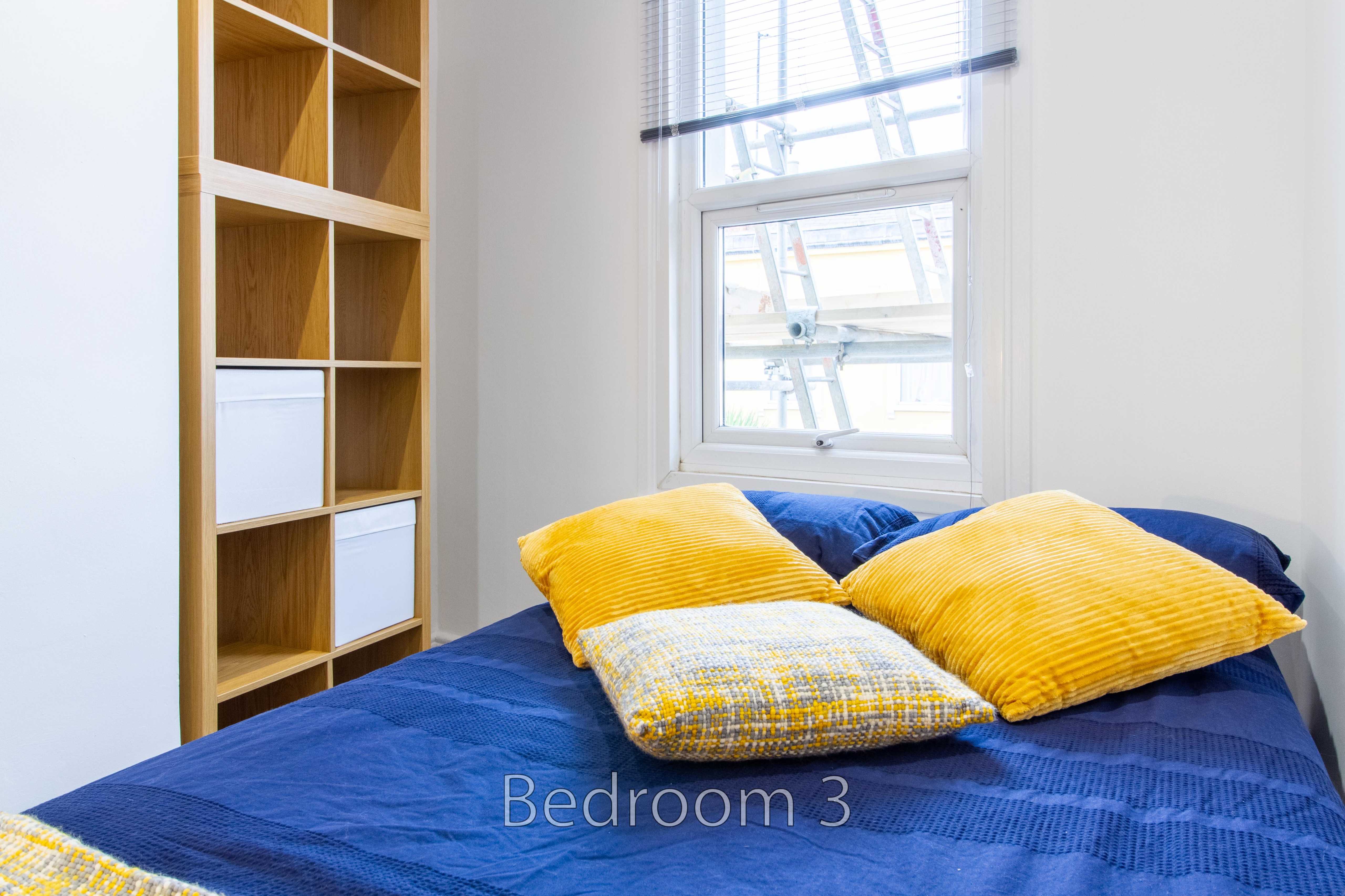 A bed with blue bedding and yellow pillows beside wooden shelving and a window.