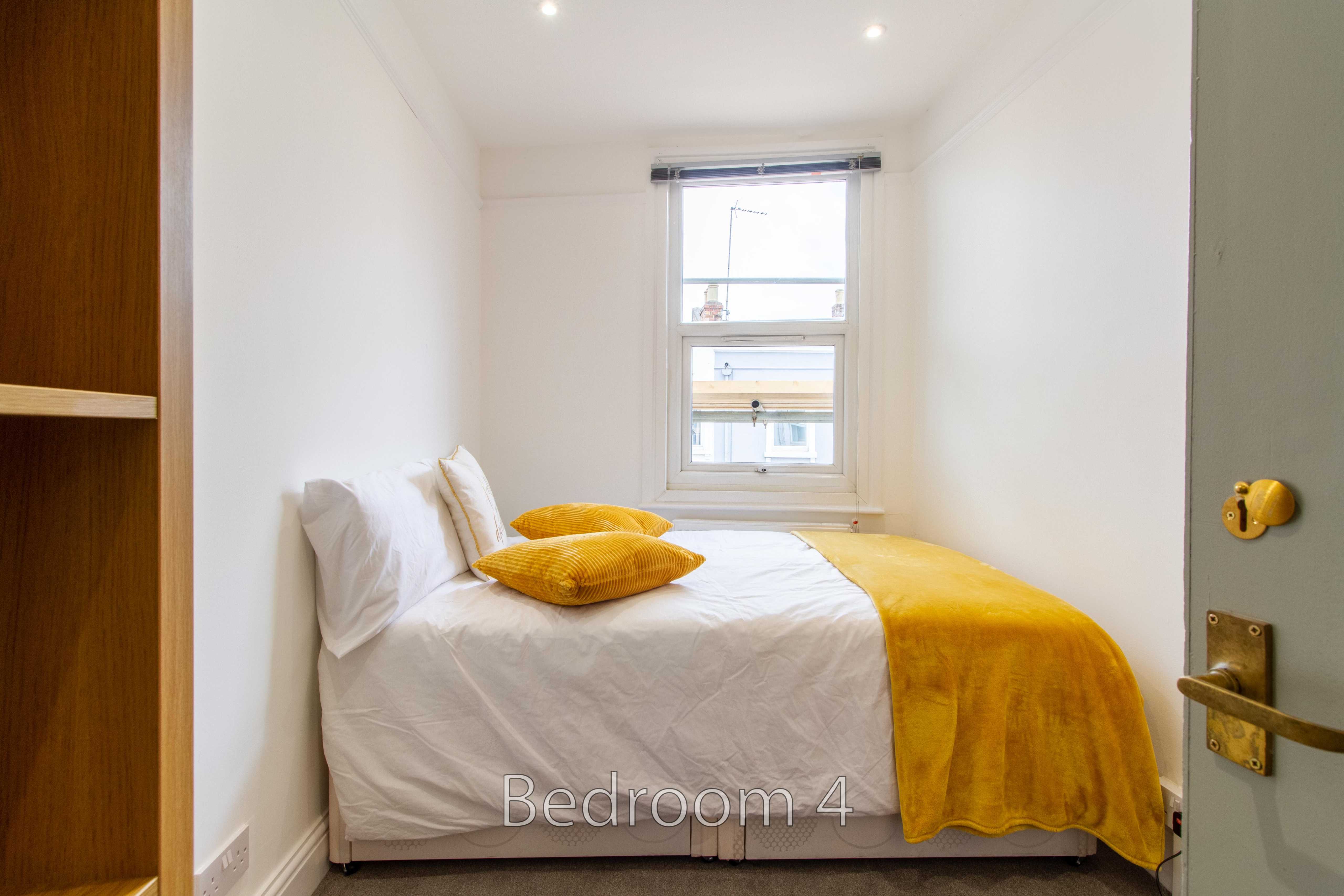 A small bedroom with a single bed, yellow bedding, a window, and built-in shelving.