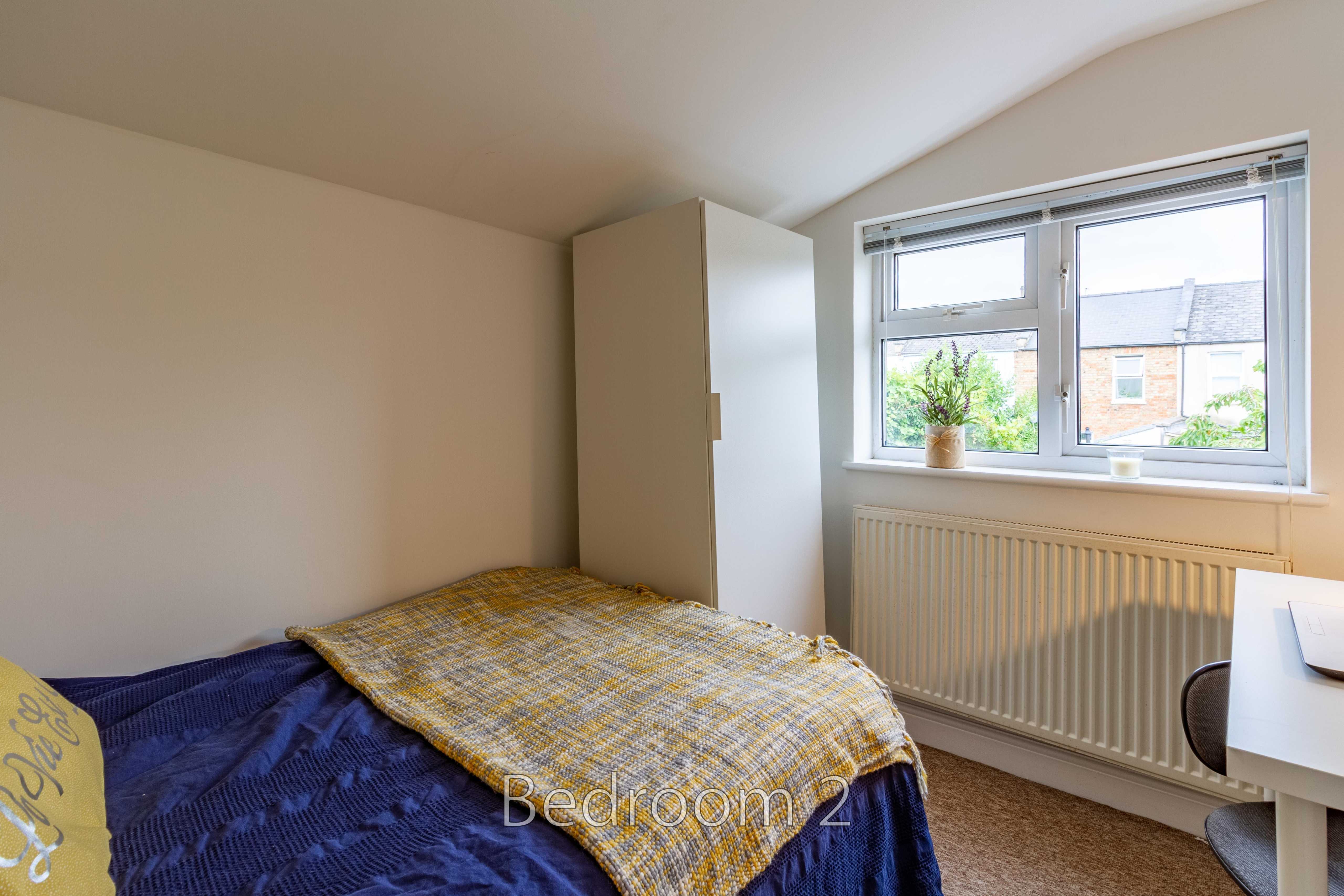A bedroom with a single bed, wardrobe, desk, radiator and window.