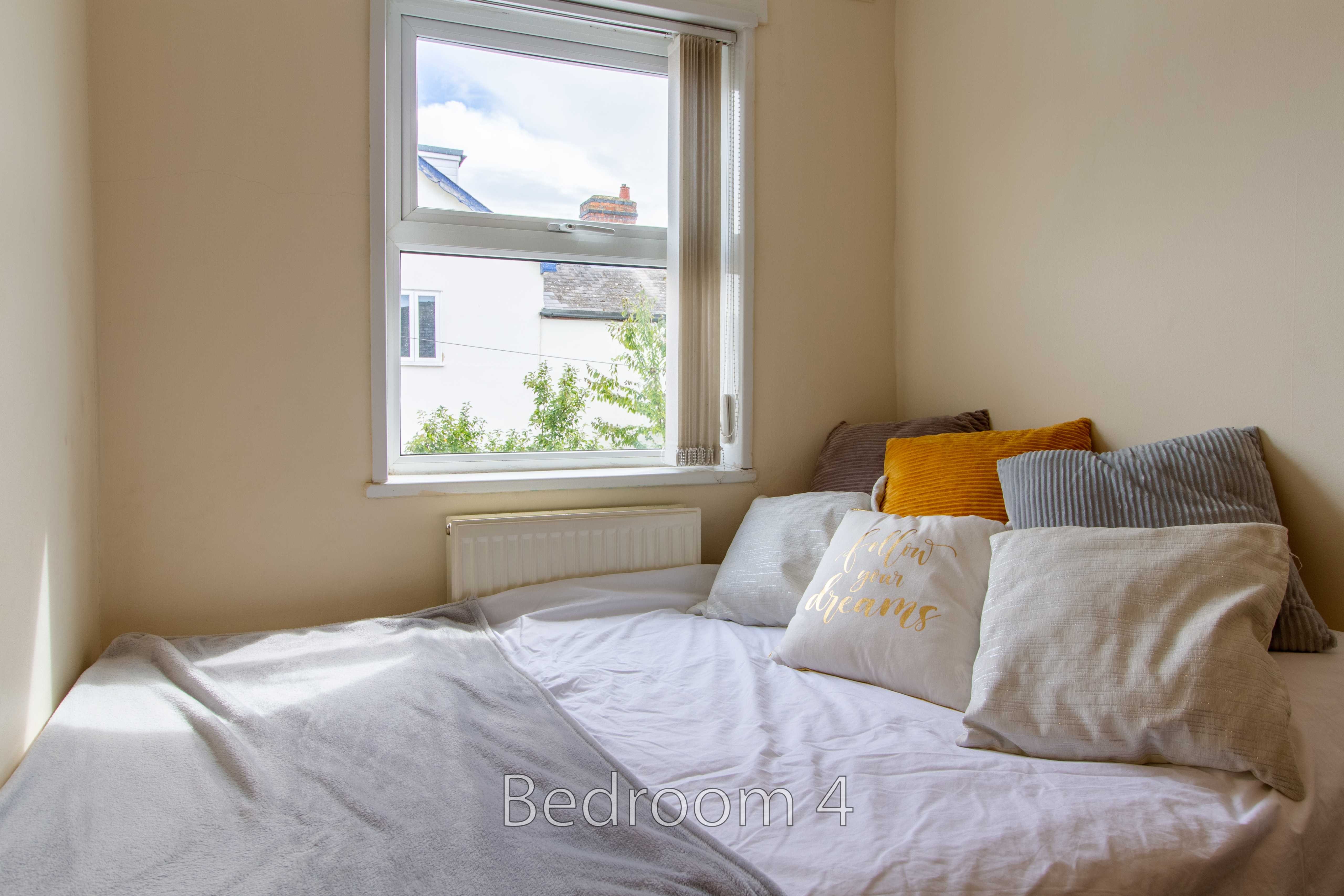 A small bedroom with a bed, cushions, a window and a radiator.