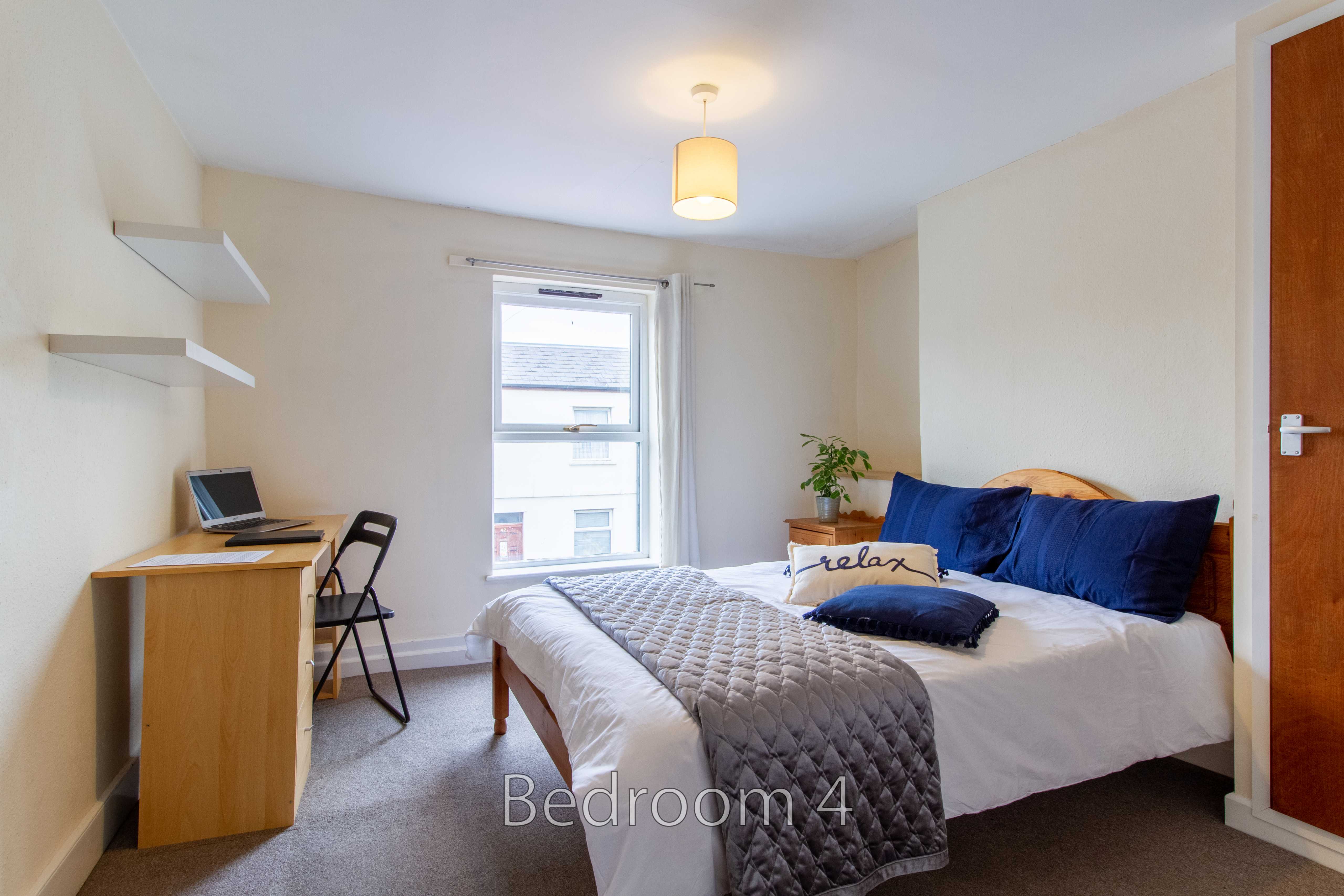 A furnished bedroom with a bed, desk, chair, window and wardrobe.