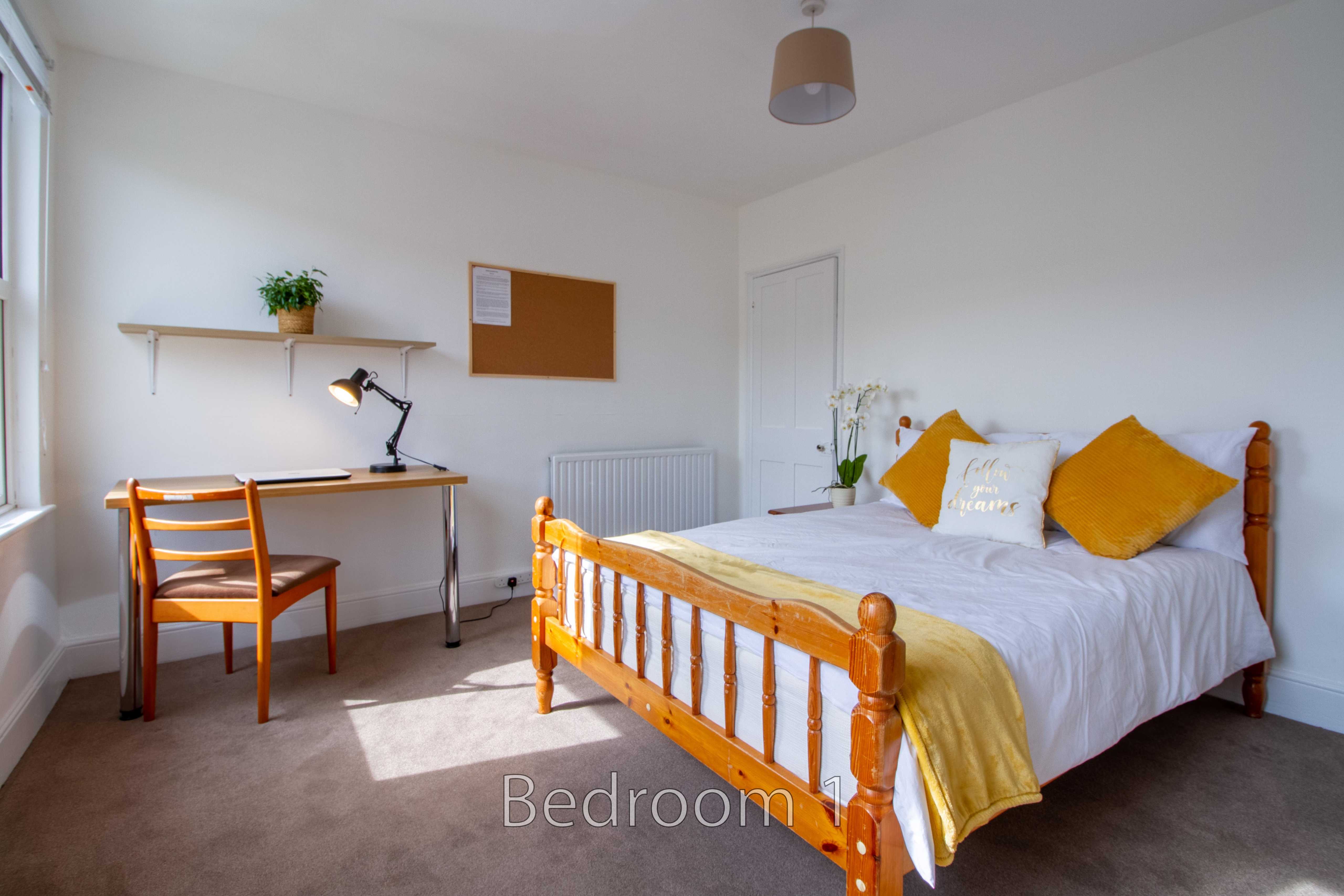 Bright bedroom with a double bed, desk, chair, radiator, window and wall shelves.