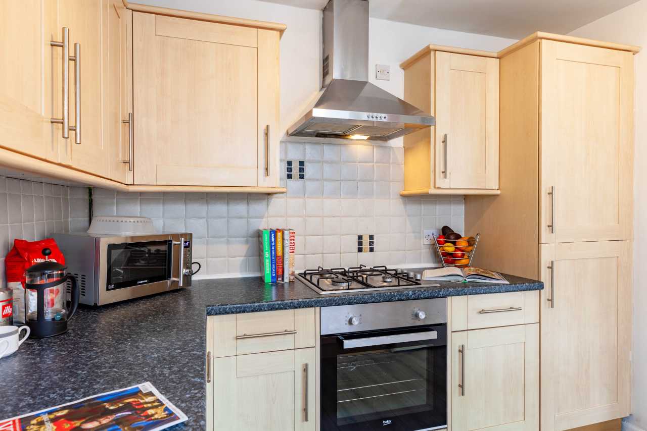 A bright fitted kitchen with wooden cabinets, tiled backsplash, countertop appliances, a gas hob and oven.