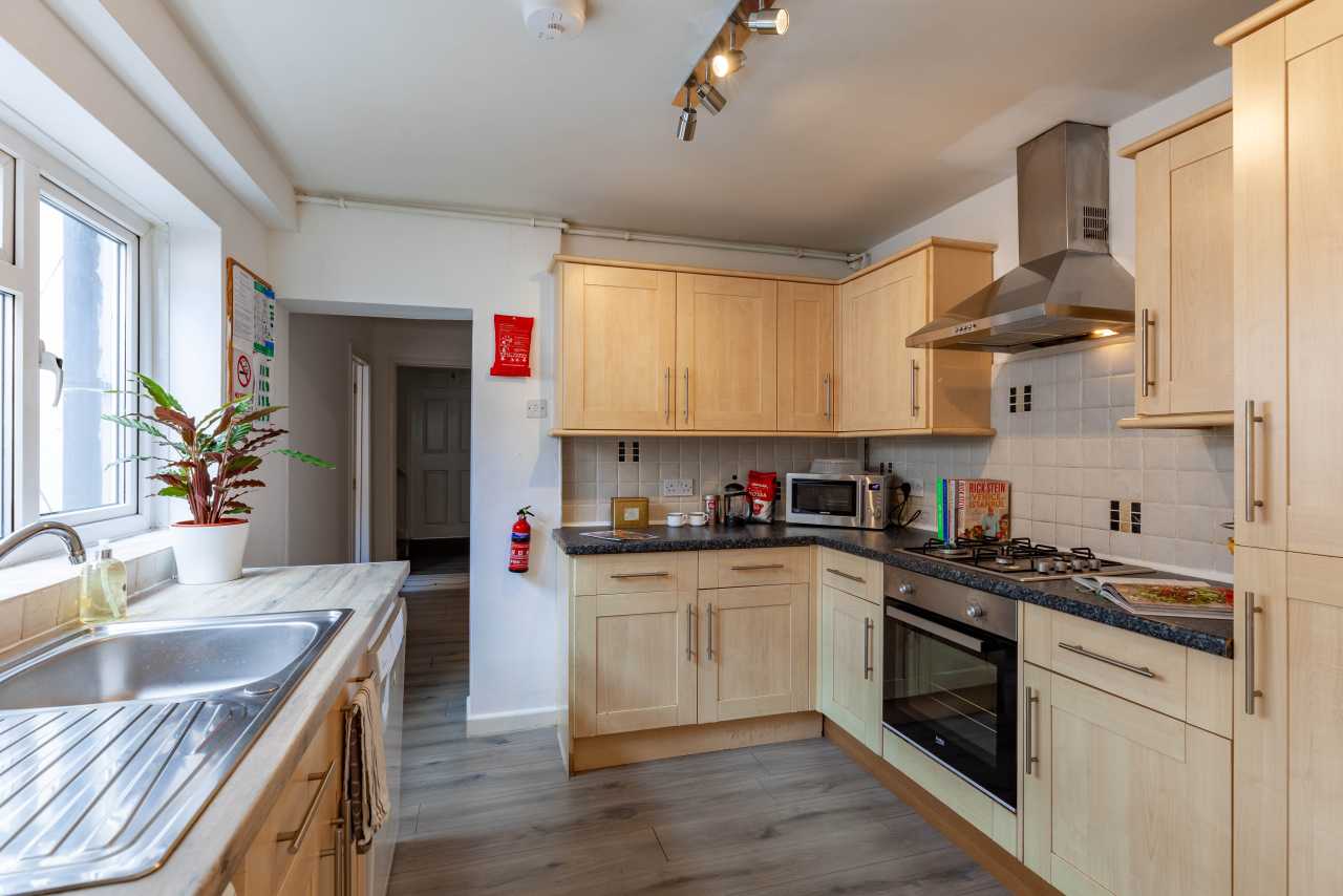 Bright fitted kitchen with wooden cabinets, sink, oven, hob, extractor hood and tiled backsplash.