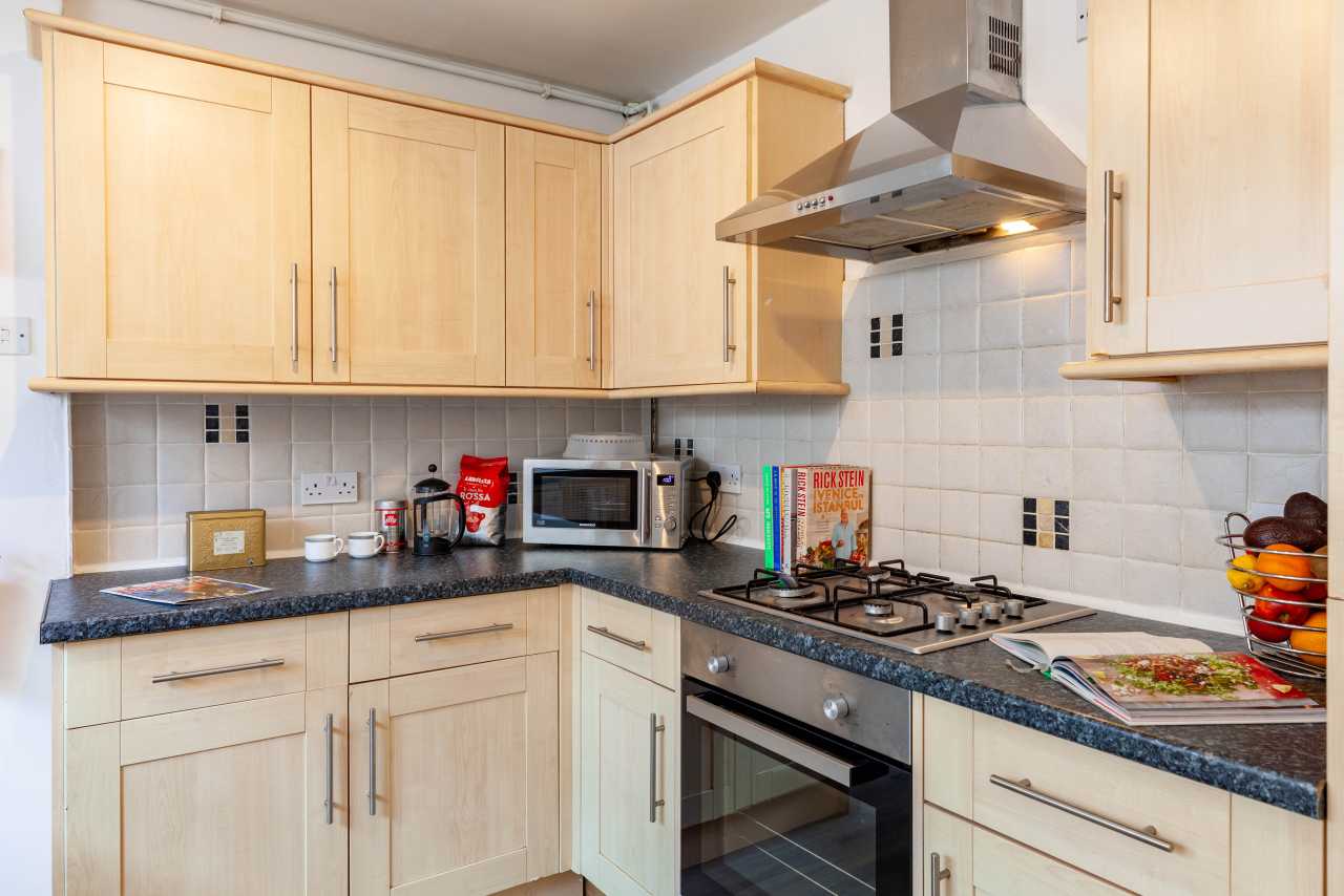 A fitted kitchen with wooden cabinets, tiled backsplash, countertops, a microwave, hob, oven and cooker hood.