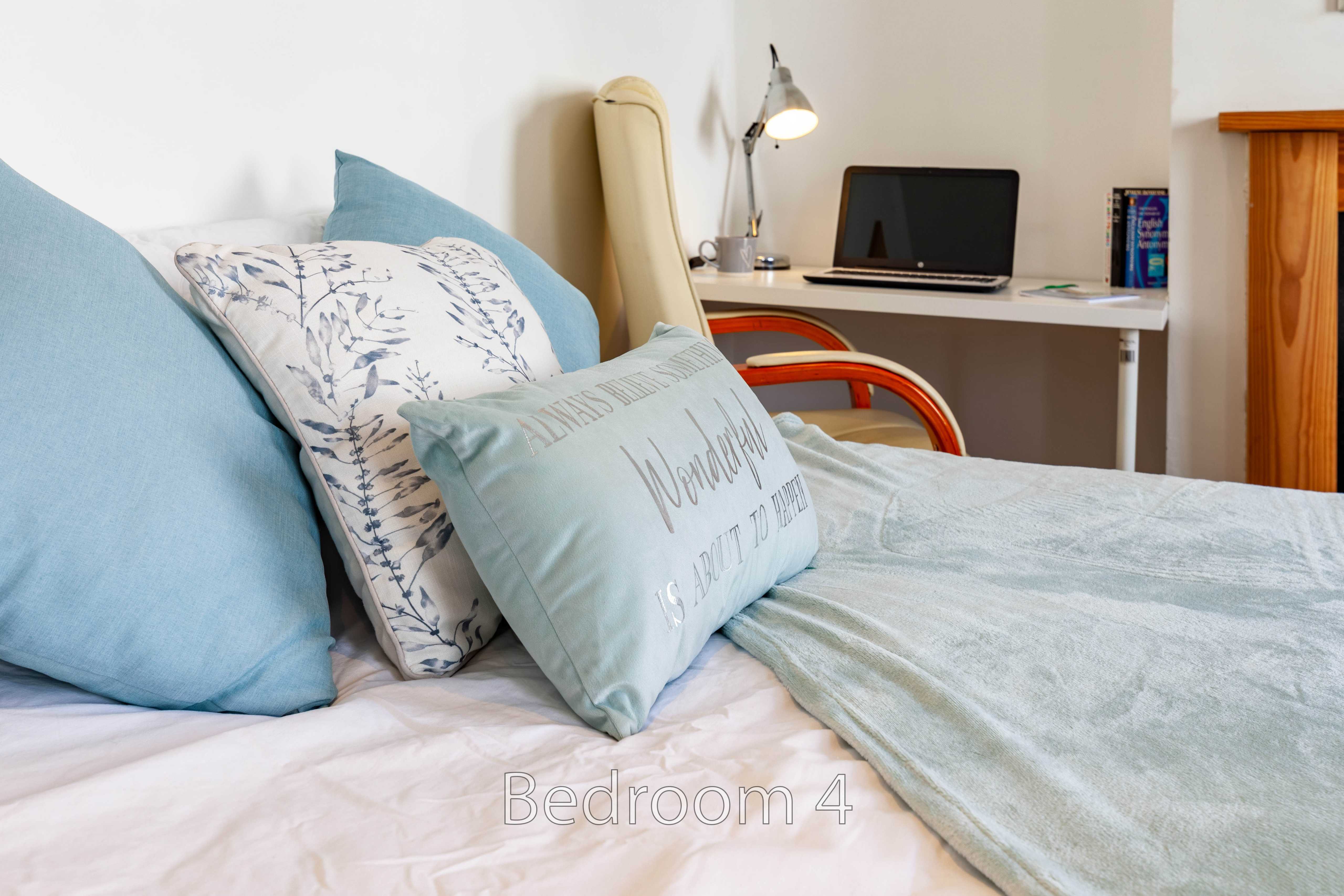 A bedroom with a made bed, blue cushions, a desk with a laptop, and a chair.